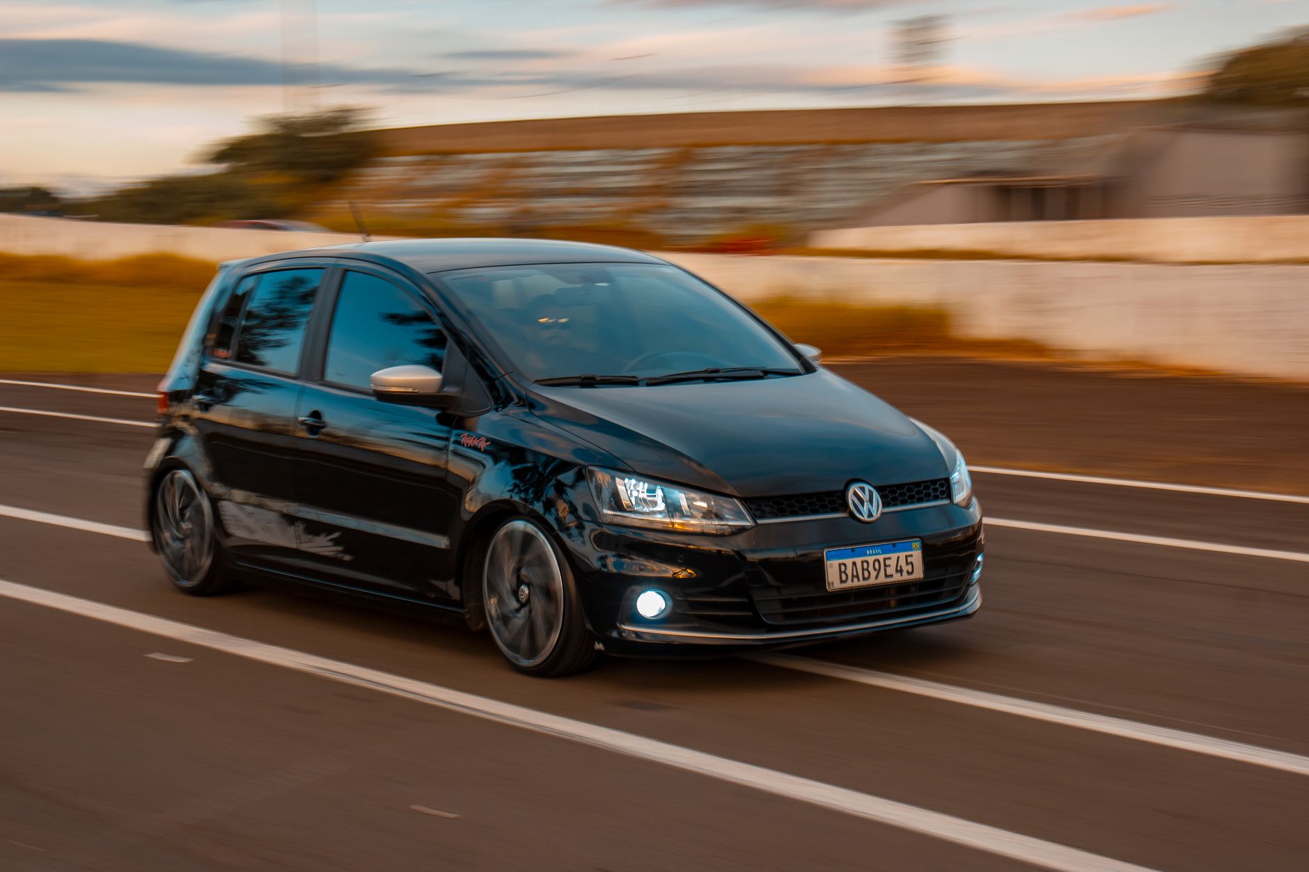 Black Volkswagen hatchback speeding on road, showcasing dynamic motion blur on a clear day.