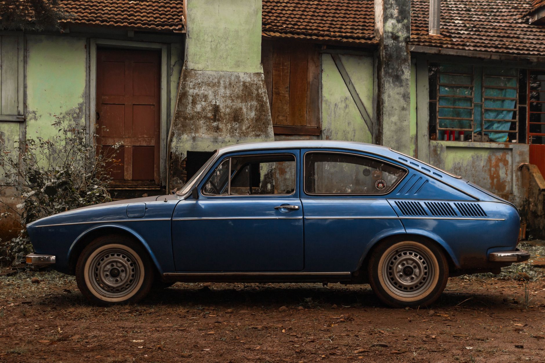 Classic blue Volkswagen car parked beside an old, rustic house with a vintage charm.