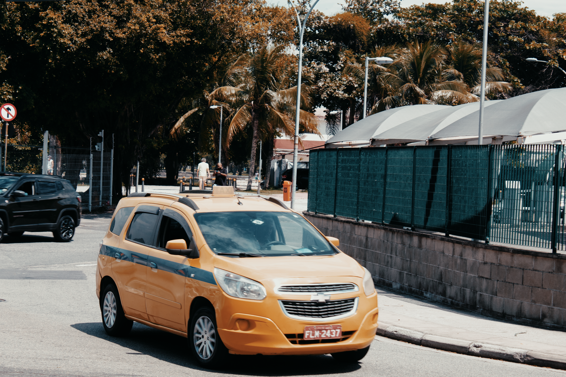A yellow taxi drives through the bustling streets of Rio de Janeiro, Brazil, under sunny skies.