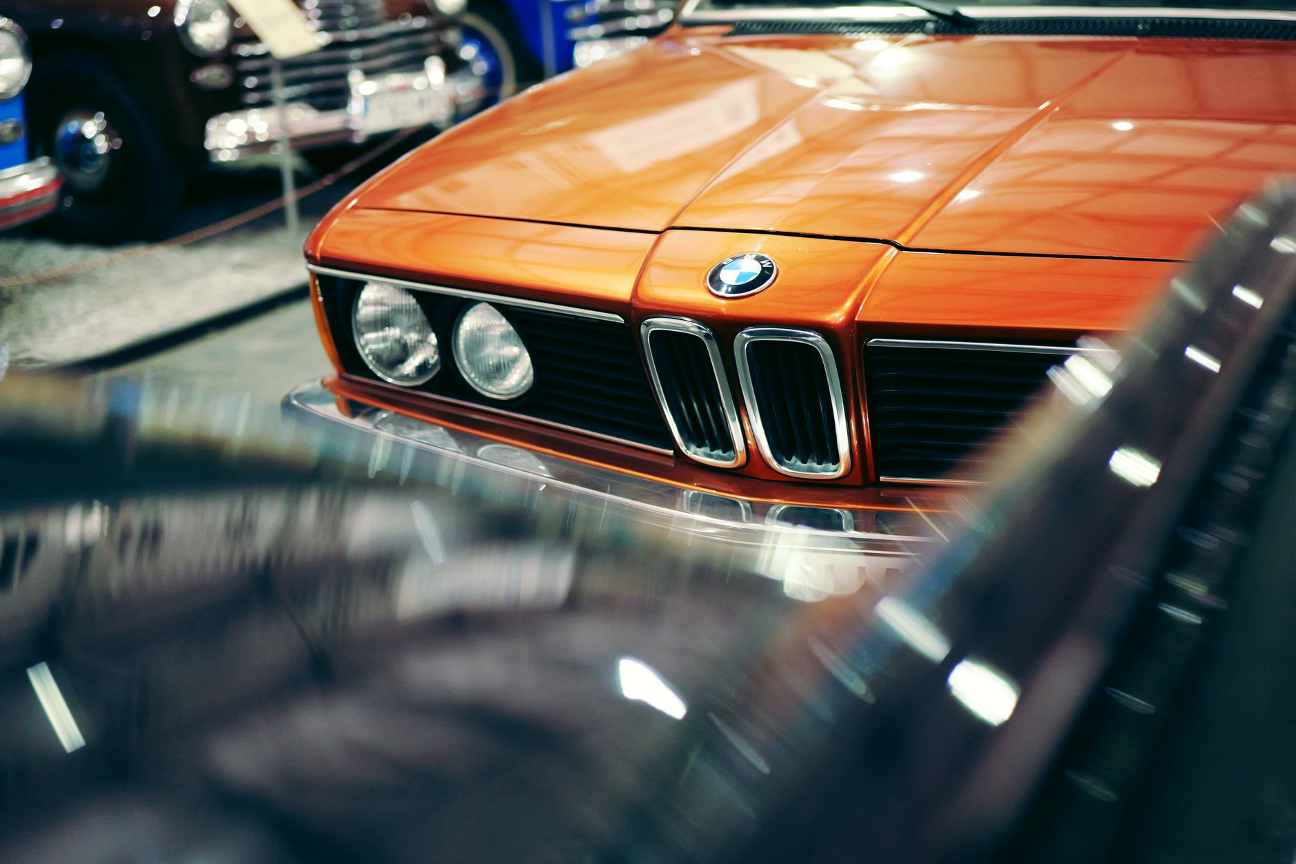 Close-up of a classic orange BMW car front in a vintage car showroom with reflections.