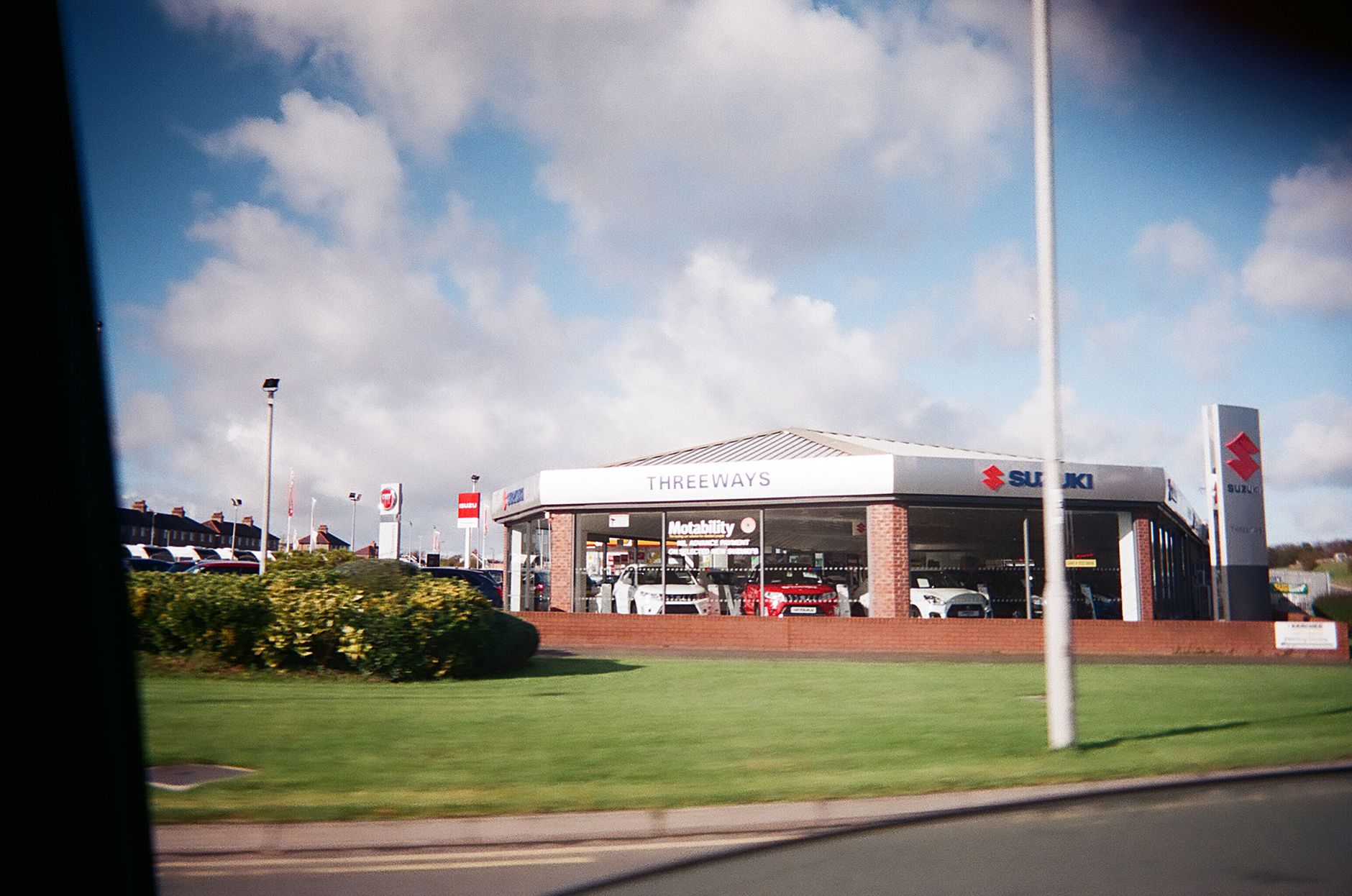Exterior view of a car dealership featuring Suzuki automobiles under a bright sky.