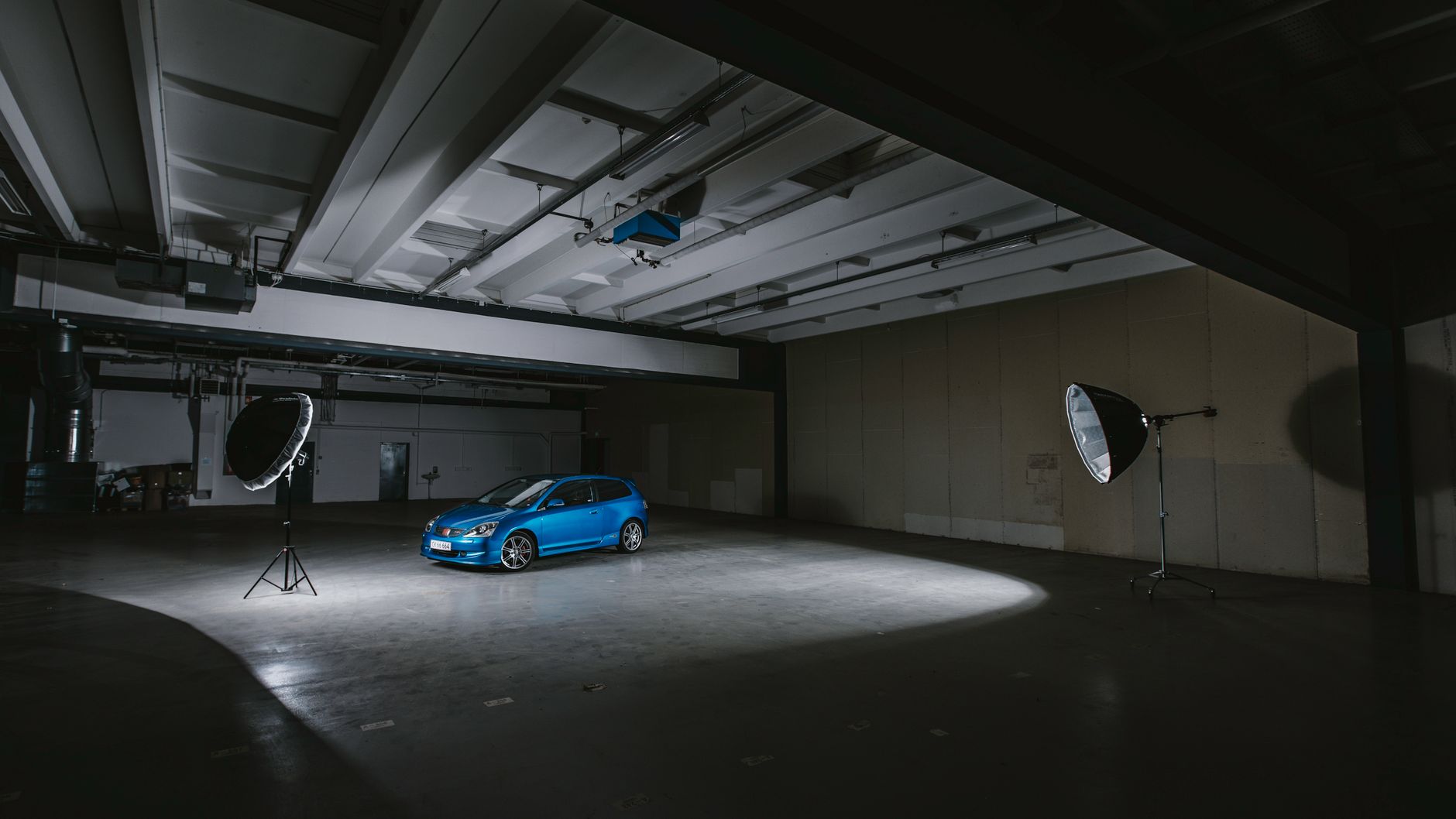 A blue car illuminated in a warehouse studio with professional lighting equipment.