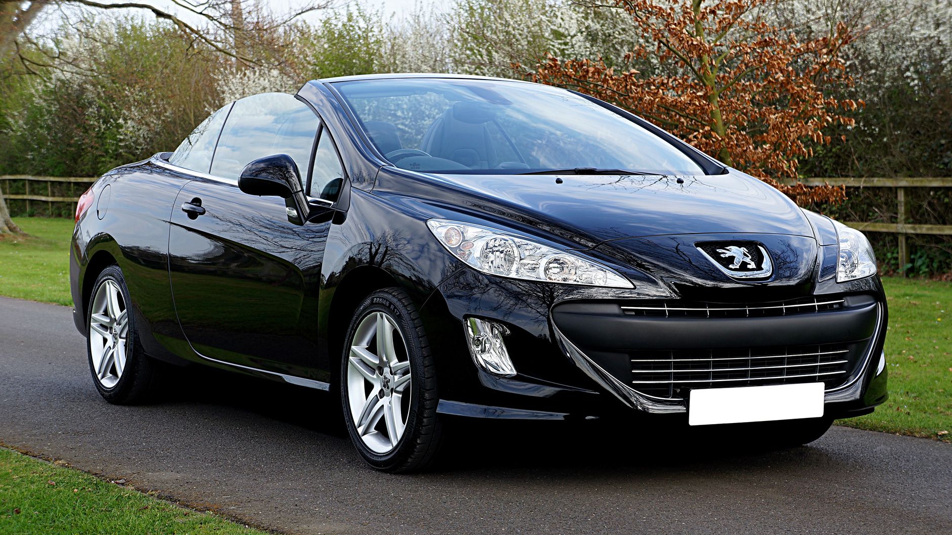 Black Peugeot 308cc convertible parked on a road in a serene outdoor setting in the UK.