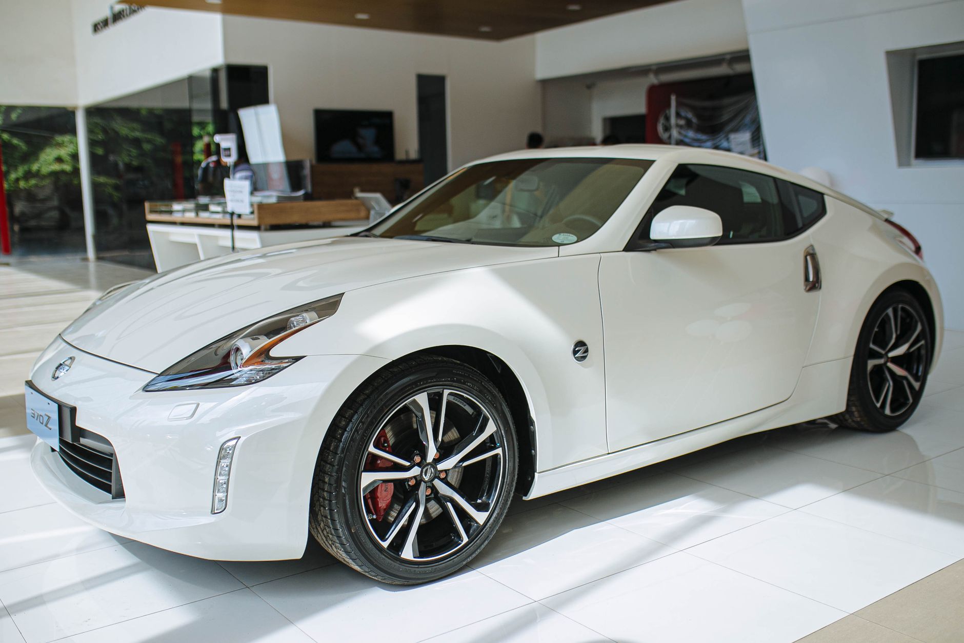 A shiny white Nissan 370Z coupe displayed in a modern car showroom, showcasing luxury and style.