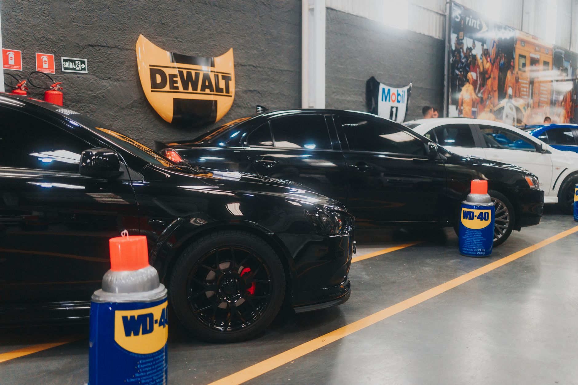 Stylish black sports cars parked in an indoor garage with WD-40 and Dewalt signage visible.