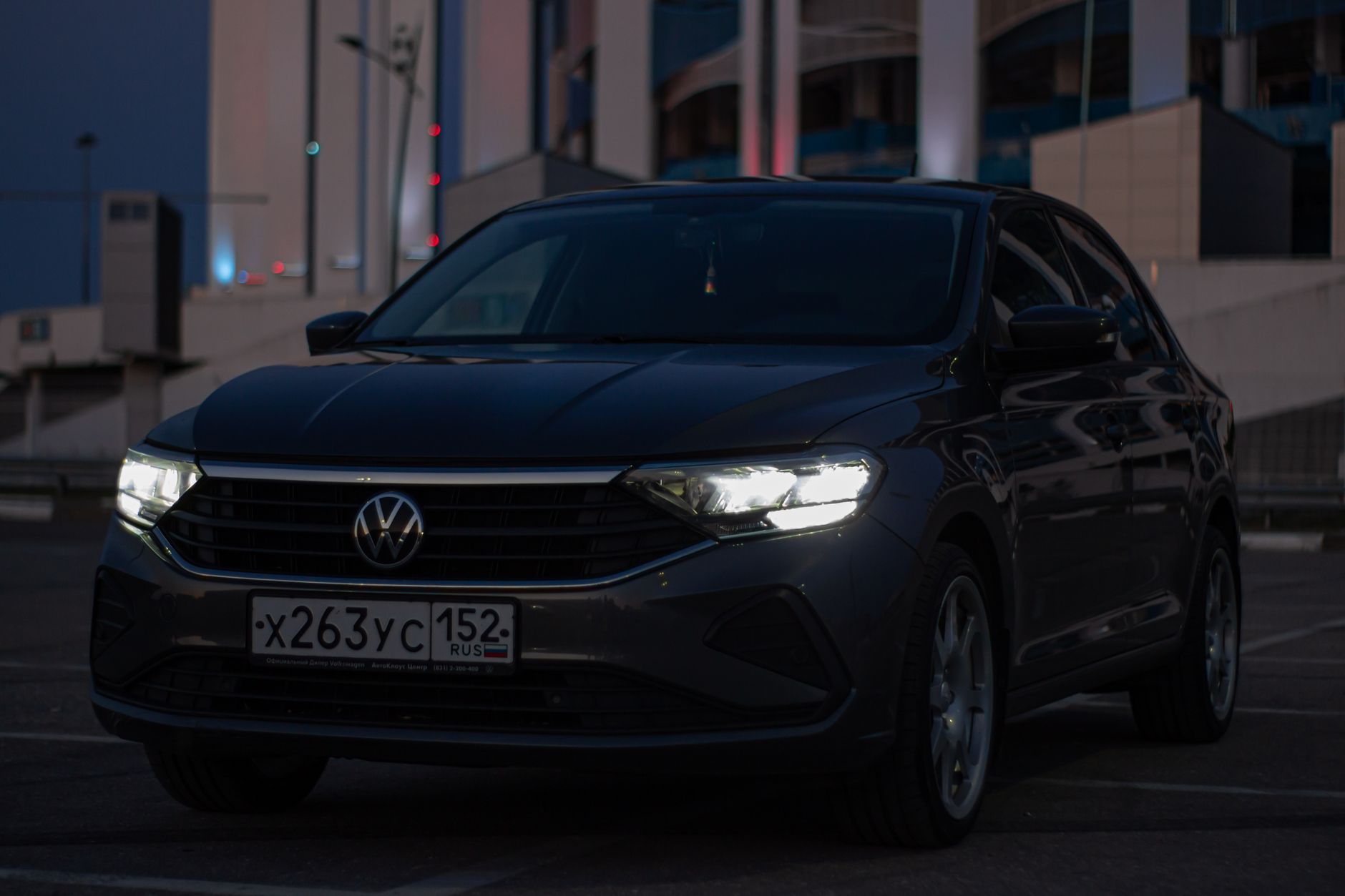 A Volkswagen car with headlights on, parked outdoors at night, showcasing a dark and moody atmosphere.