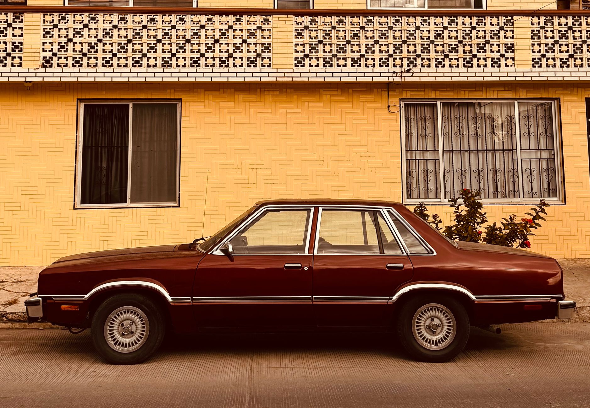 Classic maroon car parked in front of a yellow brick building, showcasing vintage style.