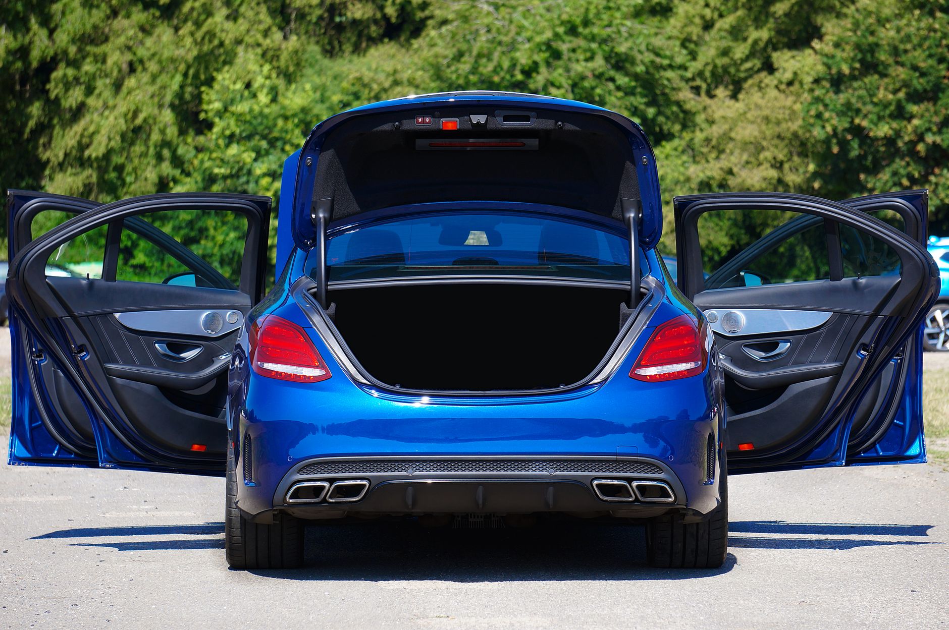 Blue luxury sedan with open doors and trunk parked in a lot.
