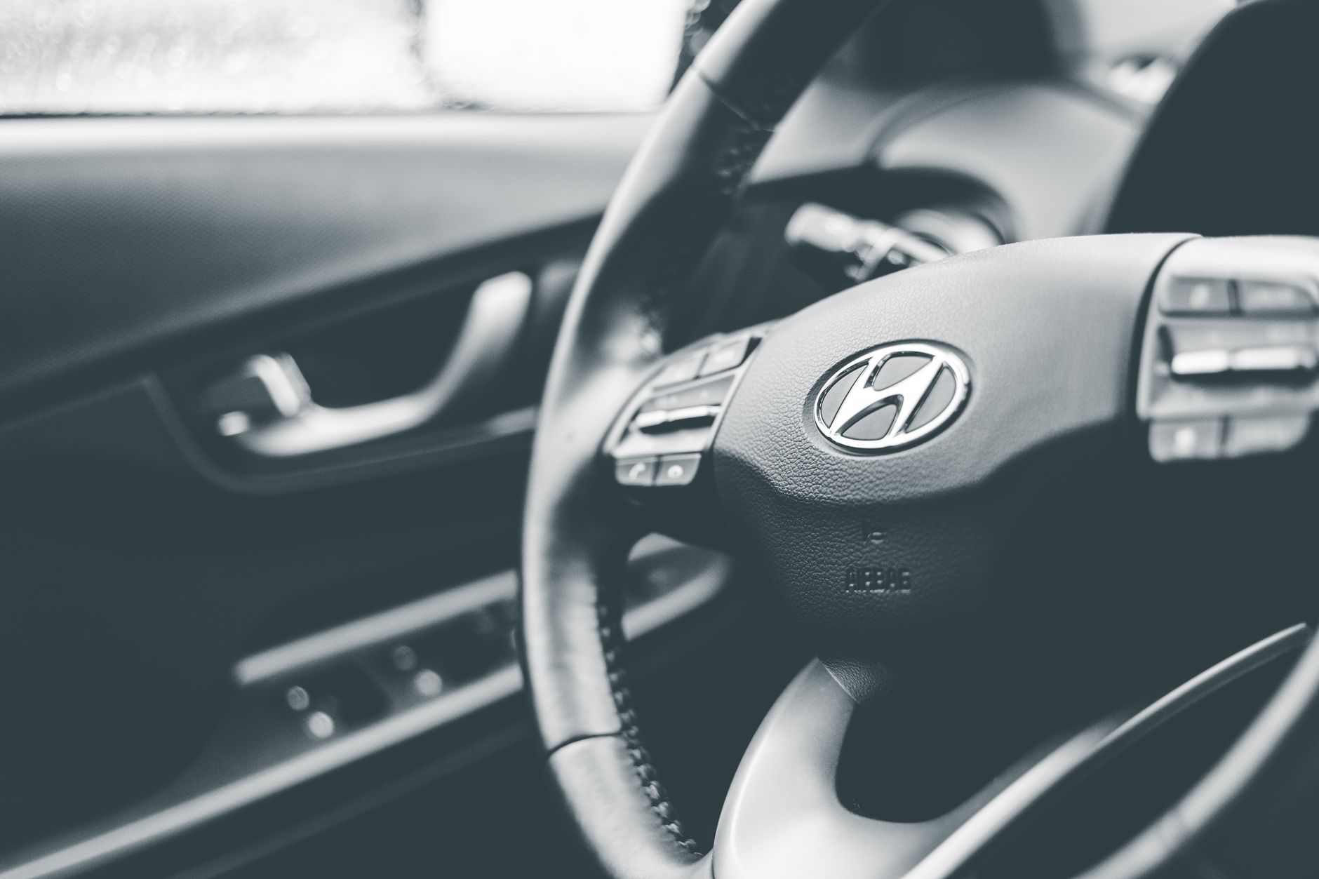 Grayscale close-up of Hyundai car steering wheel, highlighting brand interior design.