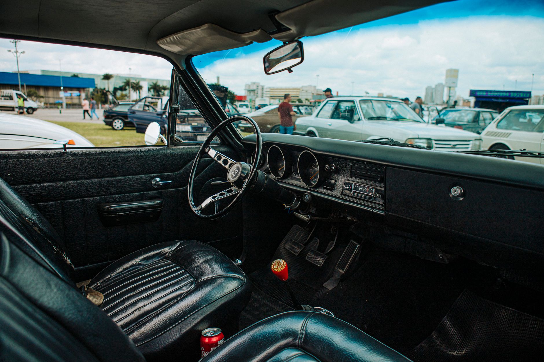 Interior of a classic car with a vintage dashboard, parked outdoors at a car show.