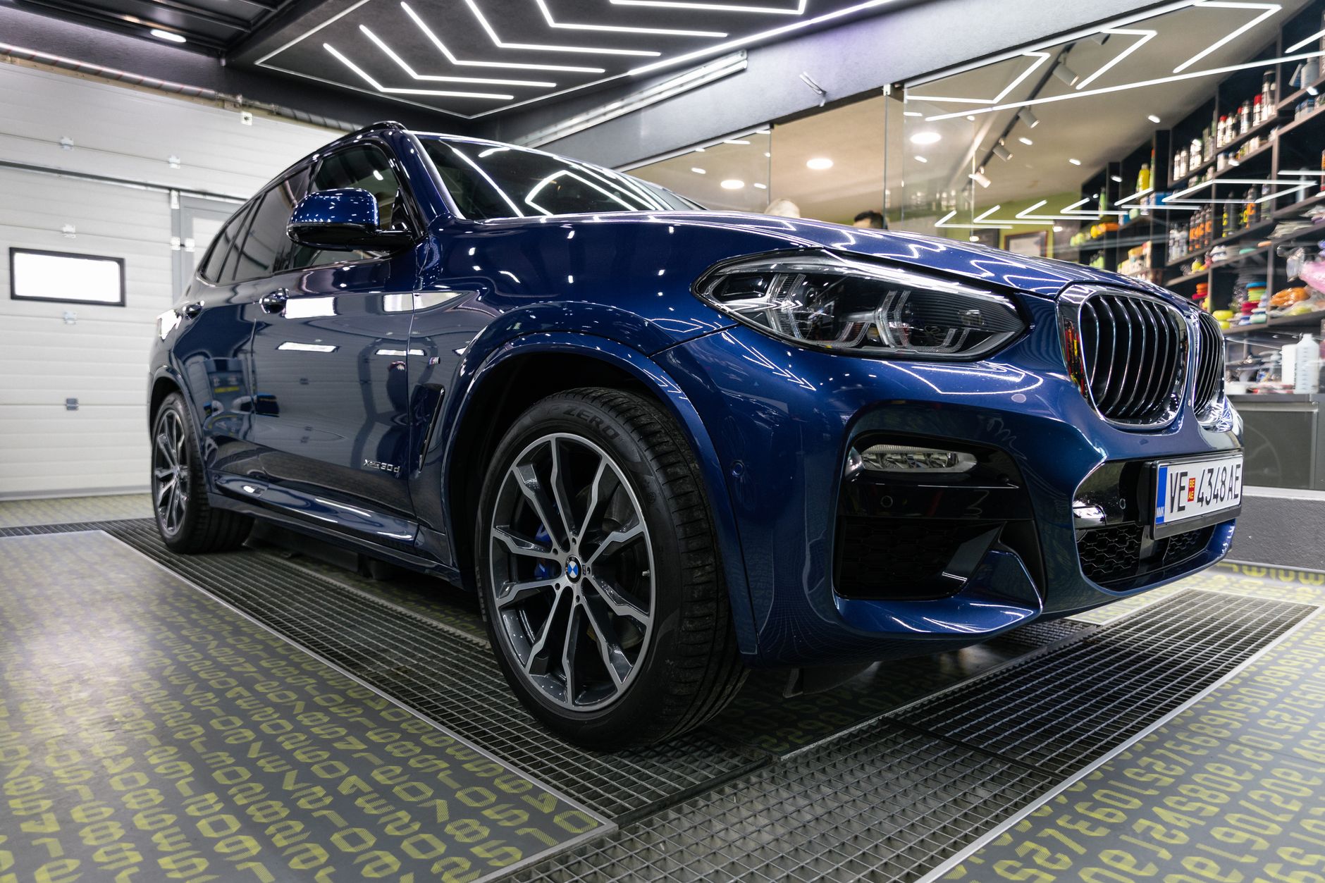 A sleek blue BMW X3 SUV showcased inside a contemporary garage setting.