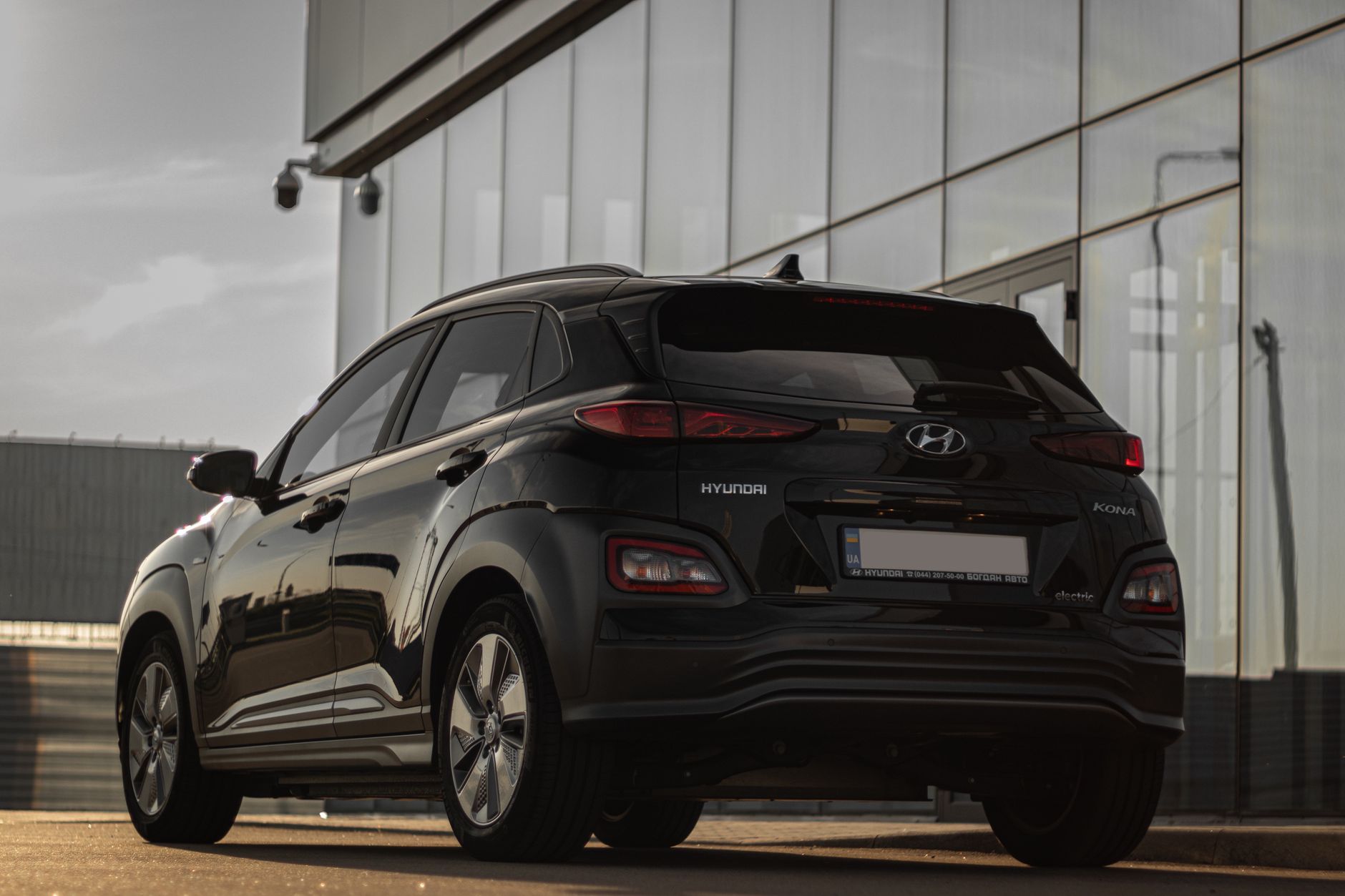 Rear view of a black Hyundai Kona parked next to a contemporary glass building reflecting urban architecture.
