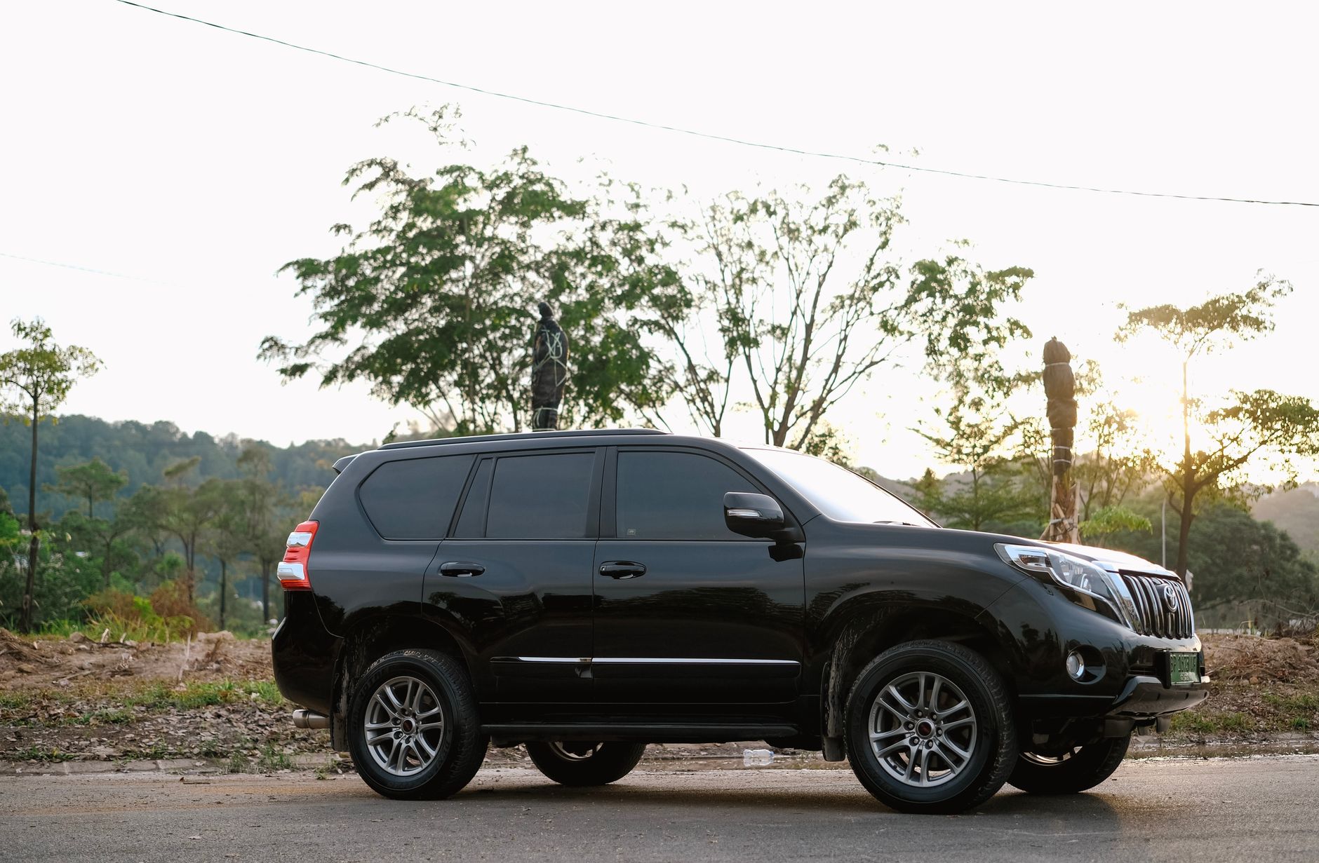 A sleek black SUV parked on a rural road with trees and a setting sun in the background.