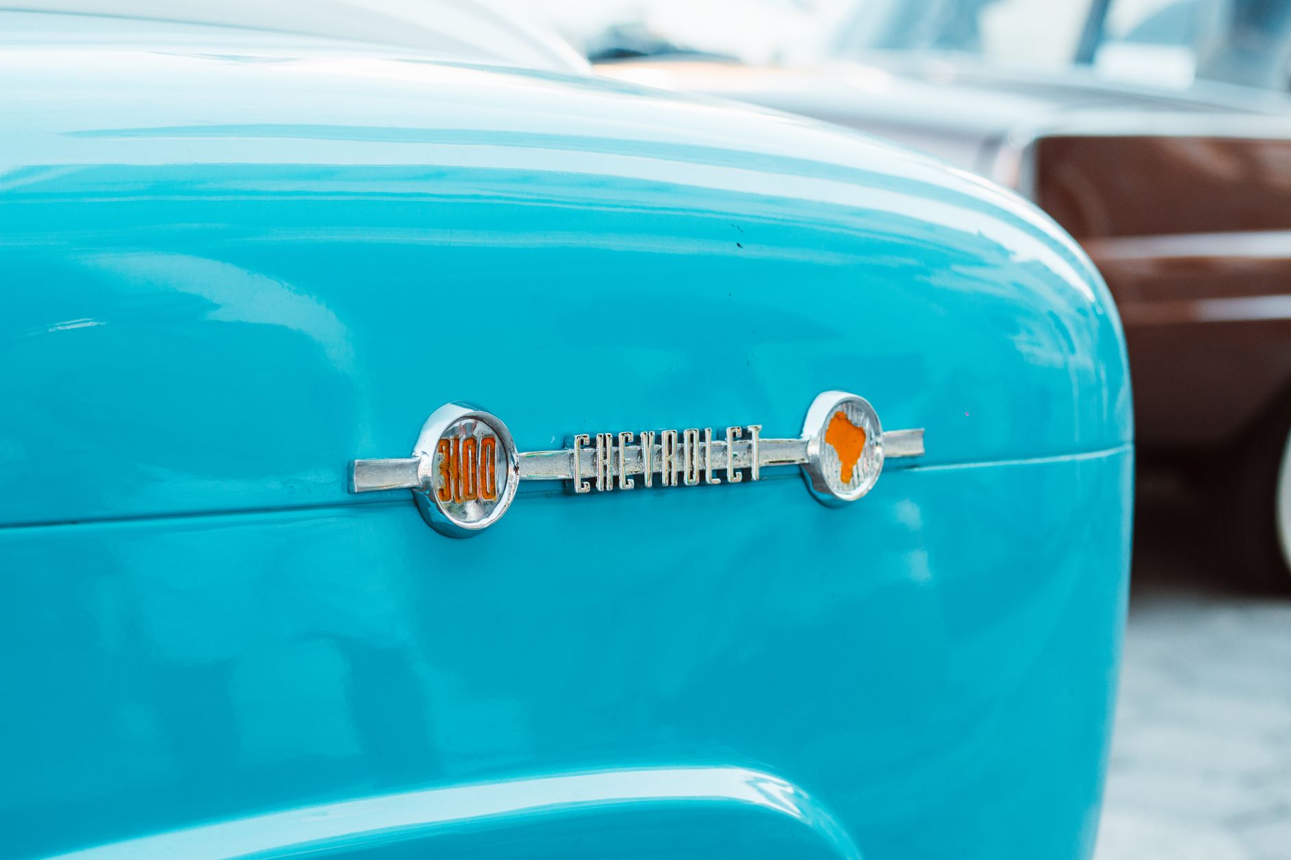 Close-up view of a vintage Chevrolet emblem on a turquoise car's body with chrome details.