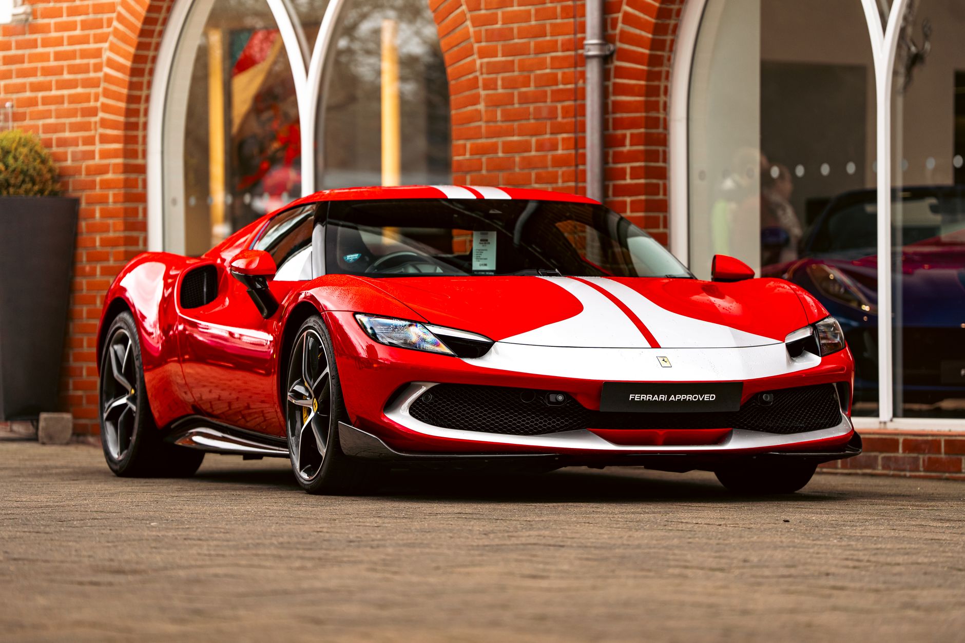 A striking red Ferrari sports car with white racing stripes displayed outdoors in Southampton showroom.