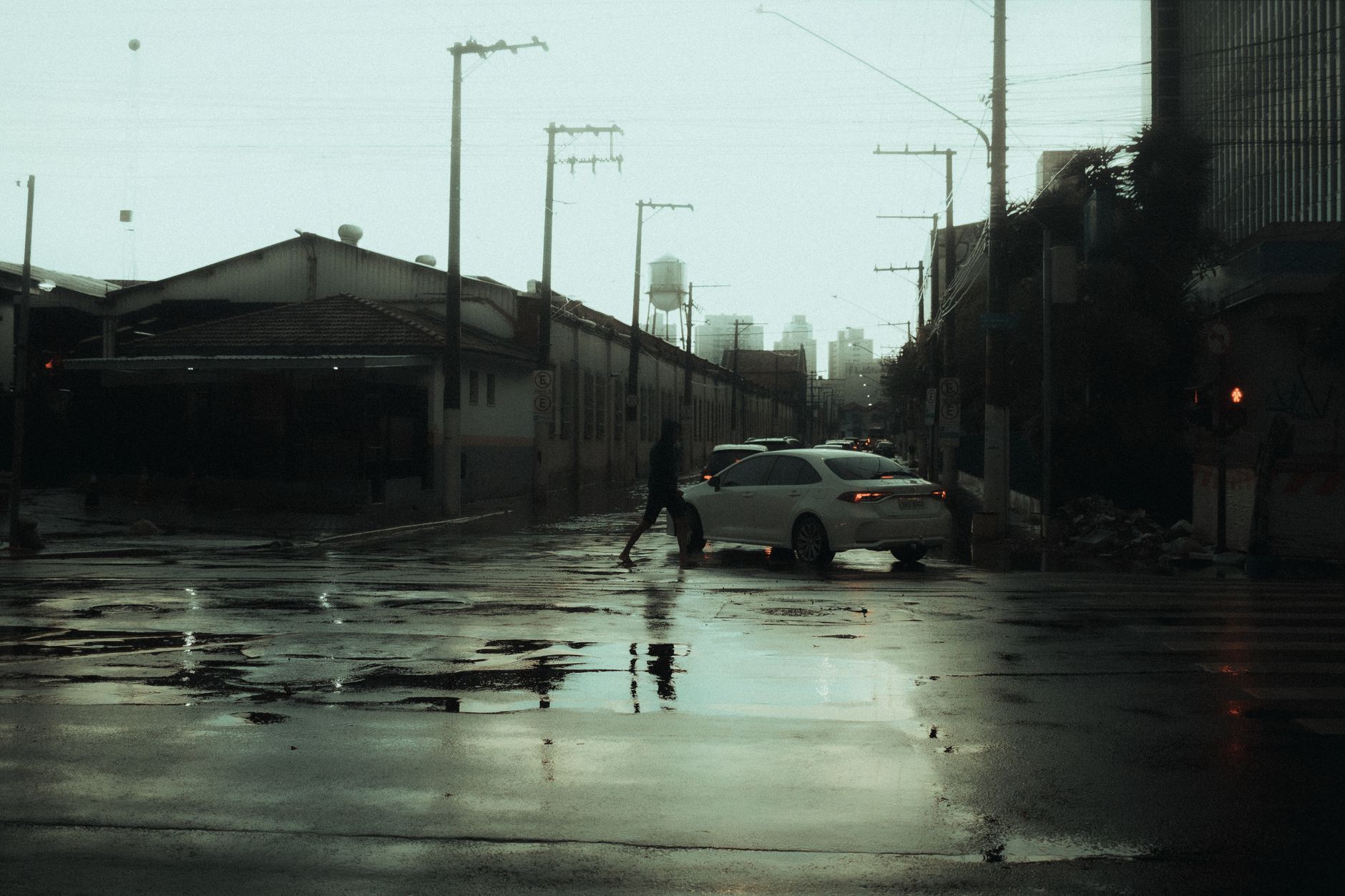 A moody urban street with rain puddles and a person crossing, captured on a rainy day.