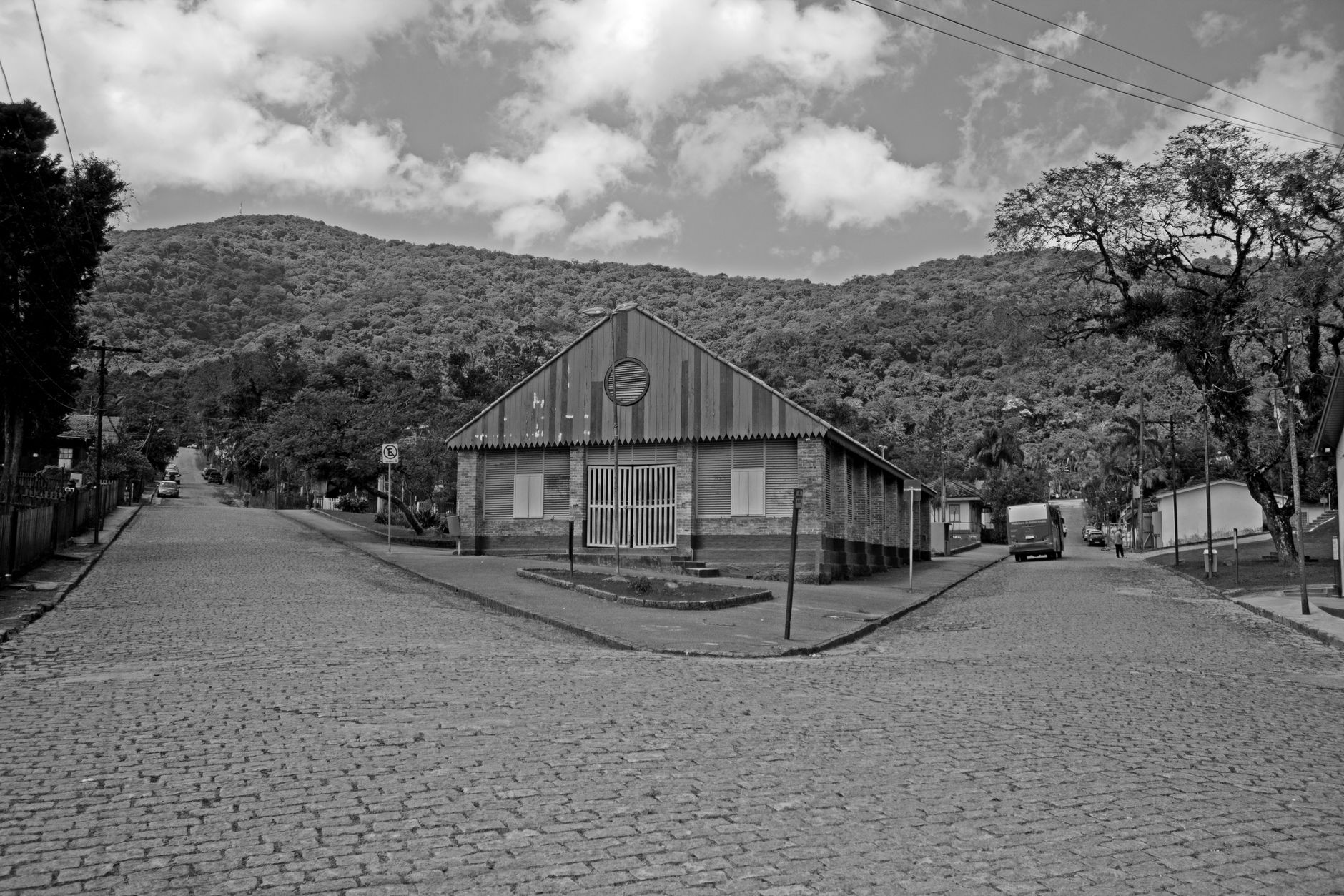 Black and white photo captures a quaint street in Paranapiacaba, São Paulo, against hilly backdrop.
