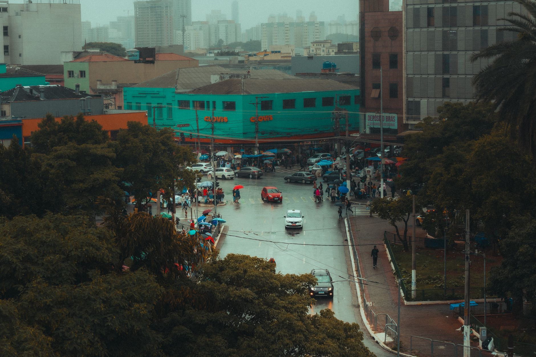 Aerial view of a bustling city intersection on a rainy day, with people and vehicles navigating the wet streets.