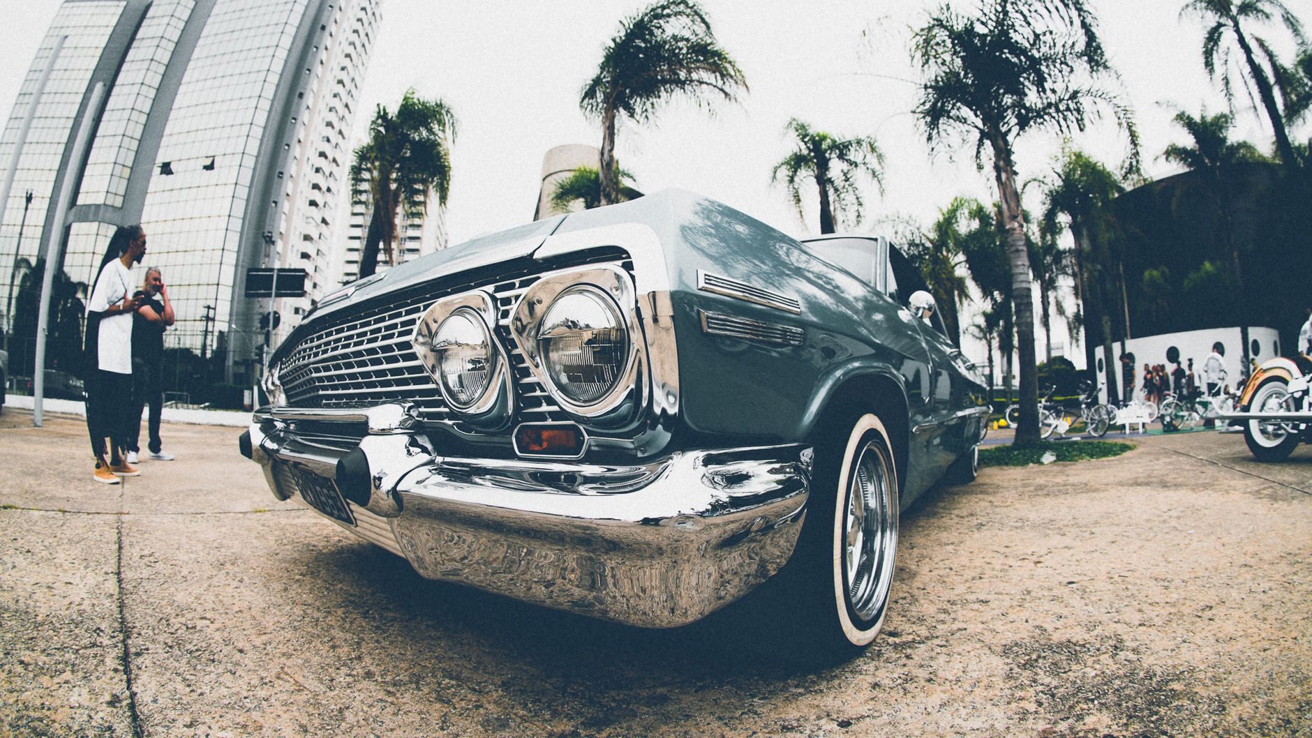 Vintage lowrider car showcased on an urban street with a cityscape backdrop and palm trees.