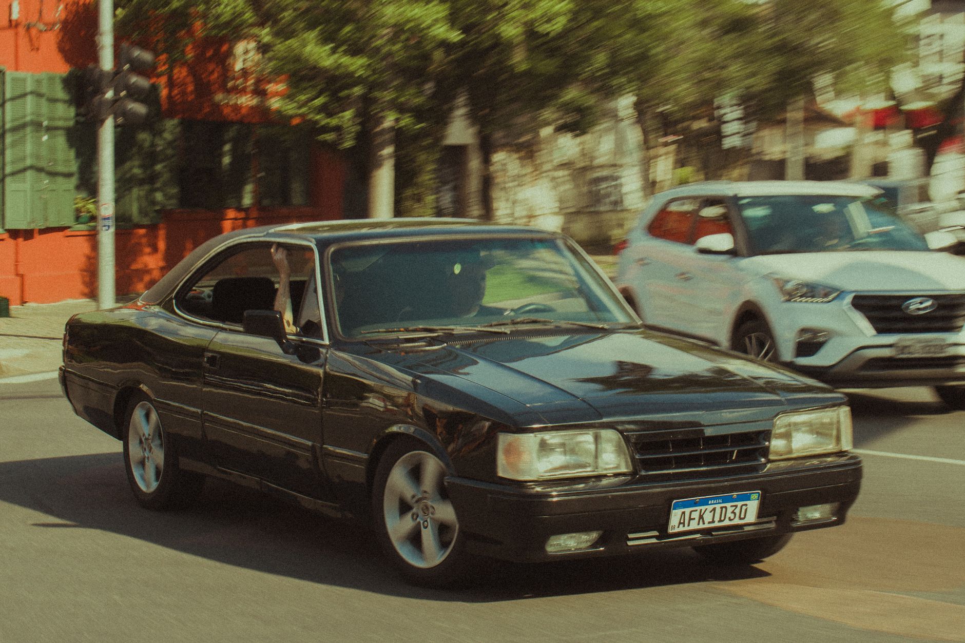 A retro black car races through a bustling city street on a sunny day.