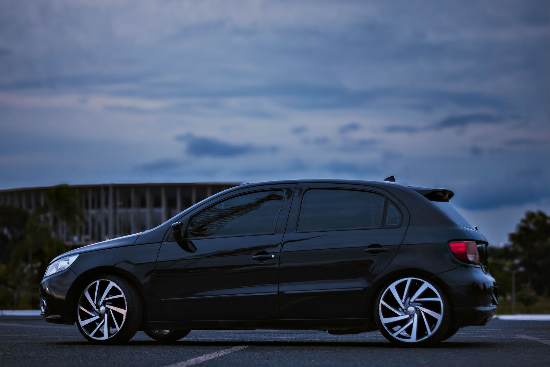 A sleek black car parked in front of Brasília's stadium at dusk.