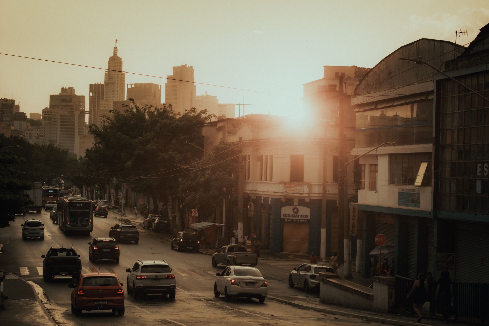 A bustling city street at sunset with cars, skyscrapers, and vibrant sunlight.
