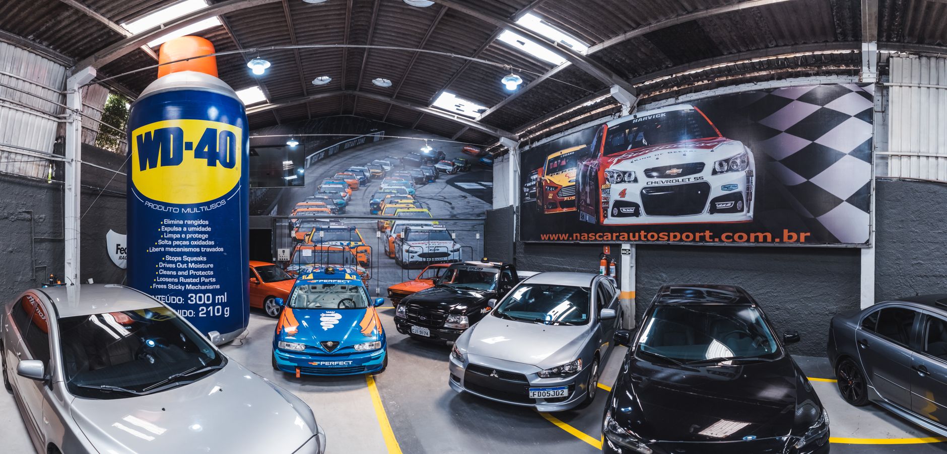 Indoor car showroom in Vila Nair, SP, Brazil, featuring a NASCAR racing-themed billboard.
