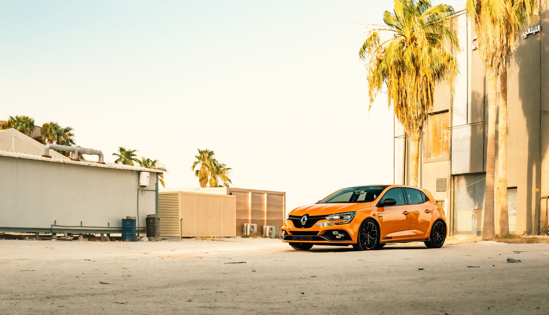 A vibrant orange car parked outdoors in Kuwait, surrounded by palm trees under a clear sky.