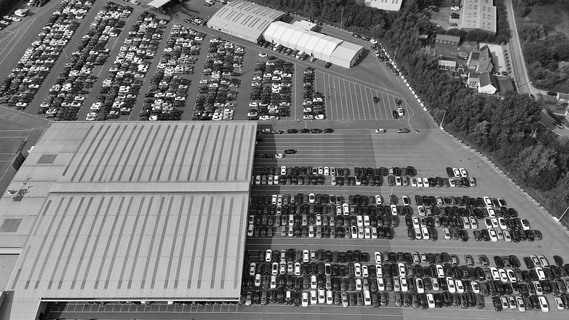 An expansive black and white aerial view of a crowded parking lot with rows of parked cars.