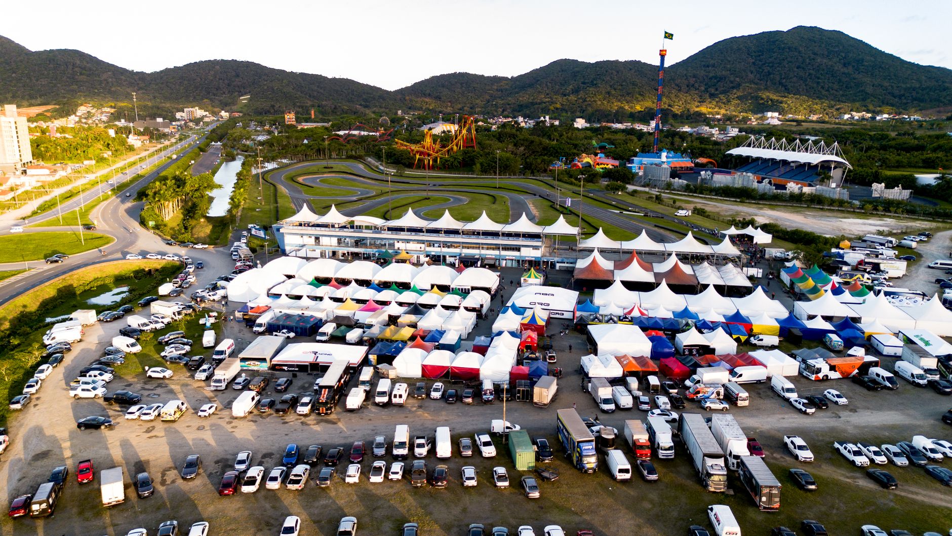 Vibrant aerial shot of a karting event with colorful tents, tracks, and vehicles under clear skies.