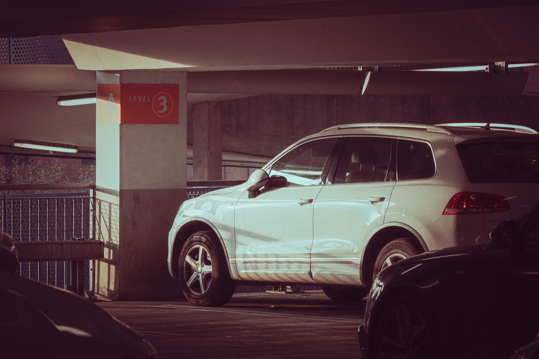 White SUV parked in a multi-level garage on level 3 with sunlight creating modern shadows.