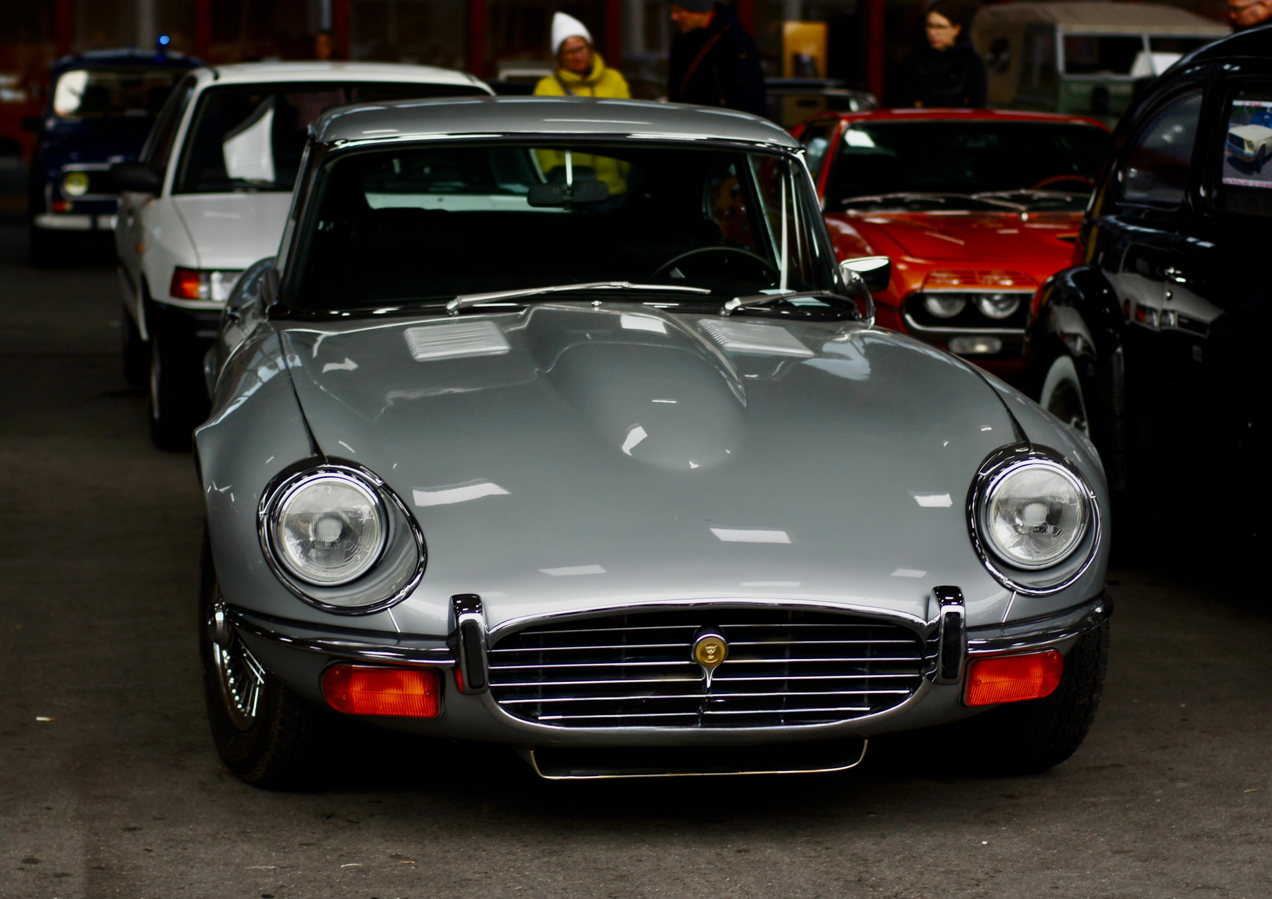 Front view of a classic Jaguar E-Type car showcased at an indoor auto show in Switzerland.