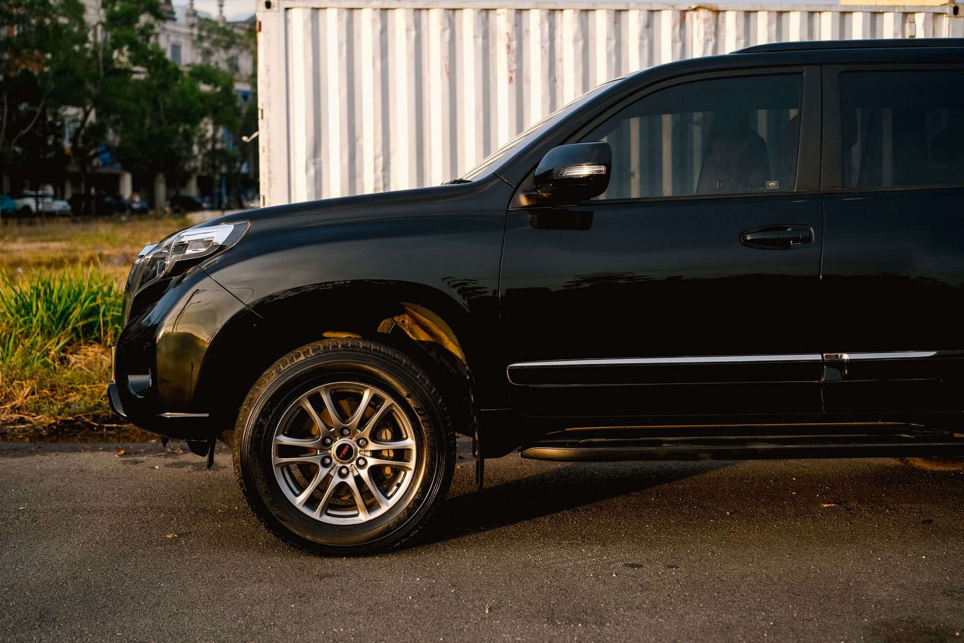 A sleek black SUV parked on the street beside a white shipping container during daytime.