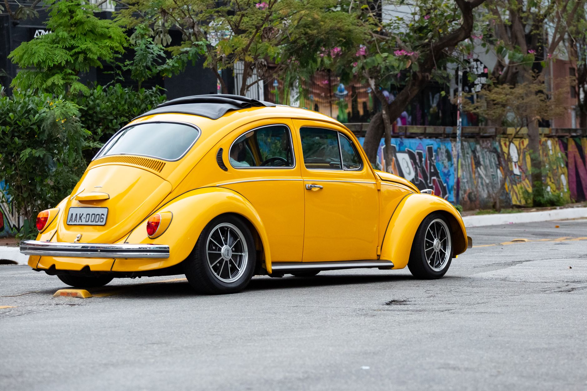 Classic yellow Volkswagen Beetle parked on a vibrant street in São Paulo, Brazil.