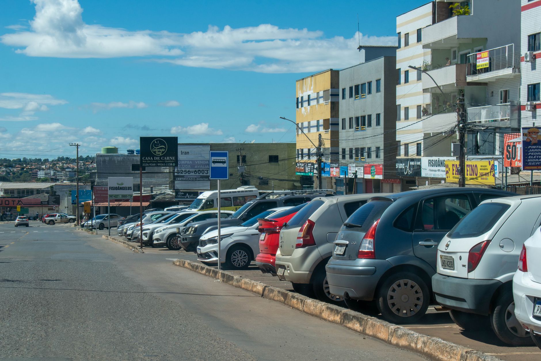 Street view in Brasilia with lined parked cars and vibrant urban buildings under a bright sky.