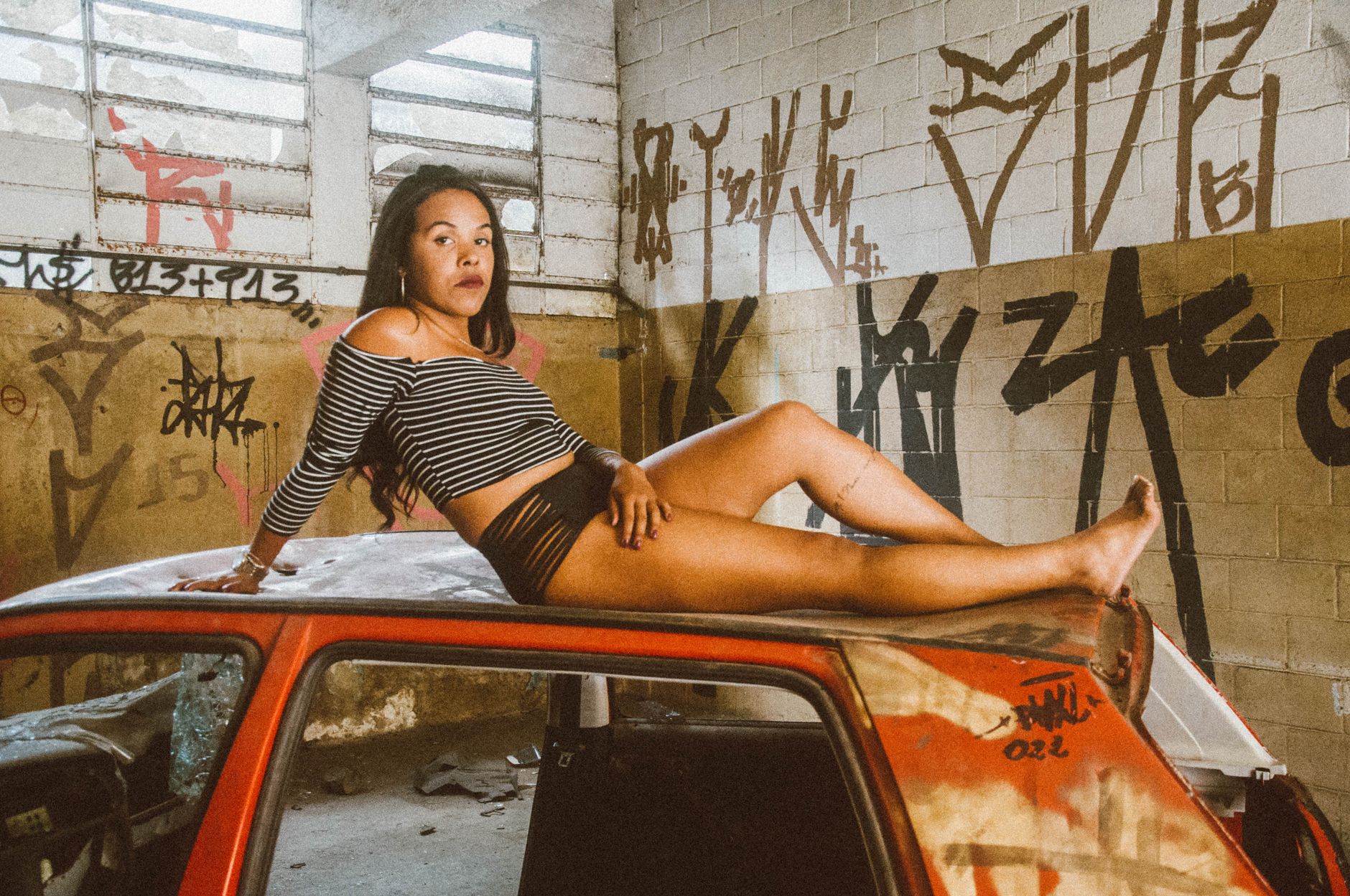 Woman posing on car in abandoned graffiti-covered urban location.