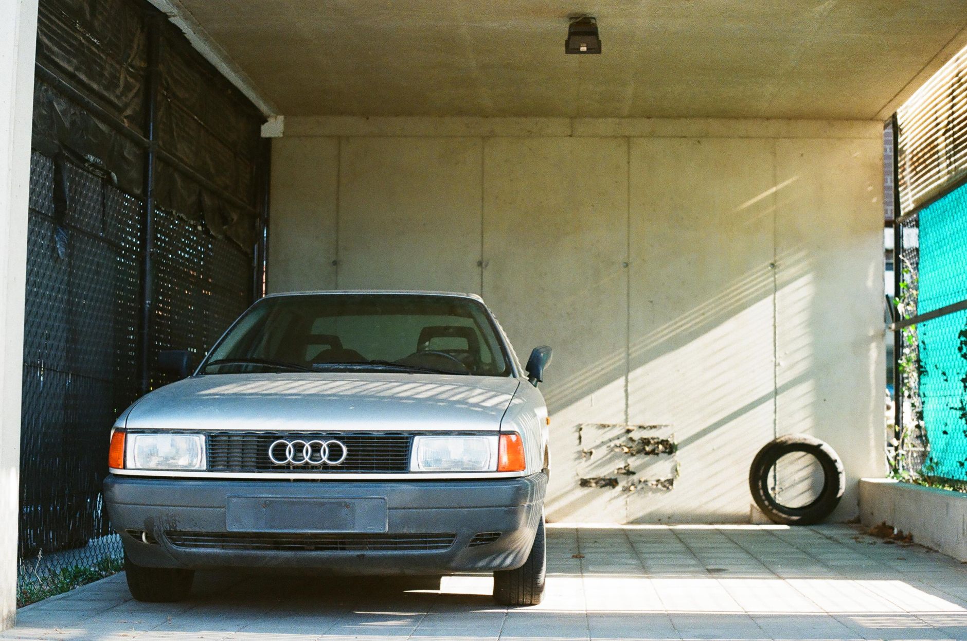 Classic car parked in a minimalist garage space with natural sunlight and shadows.