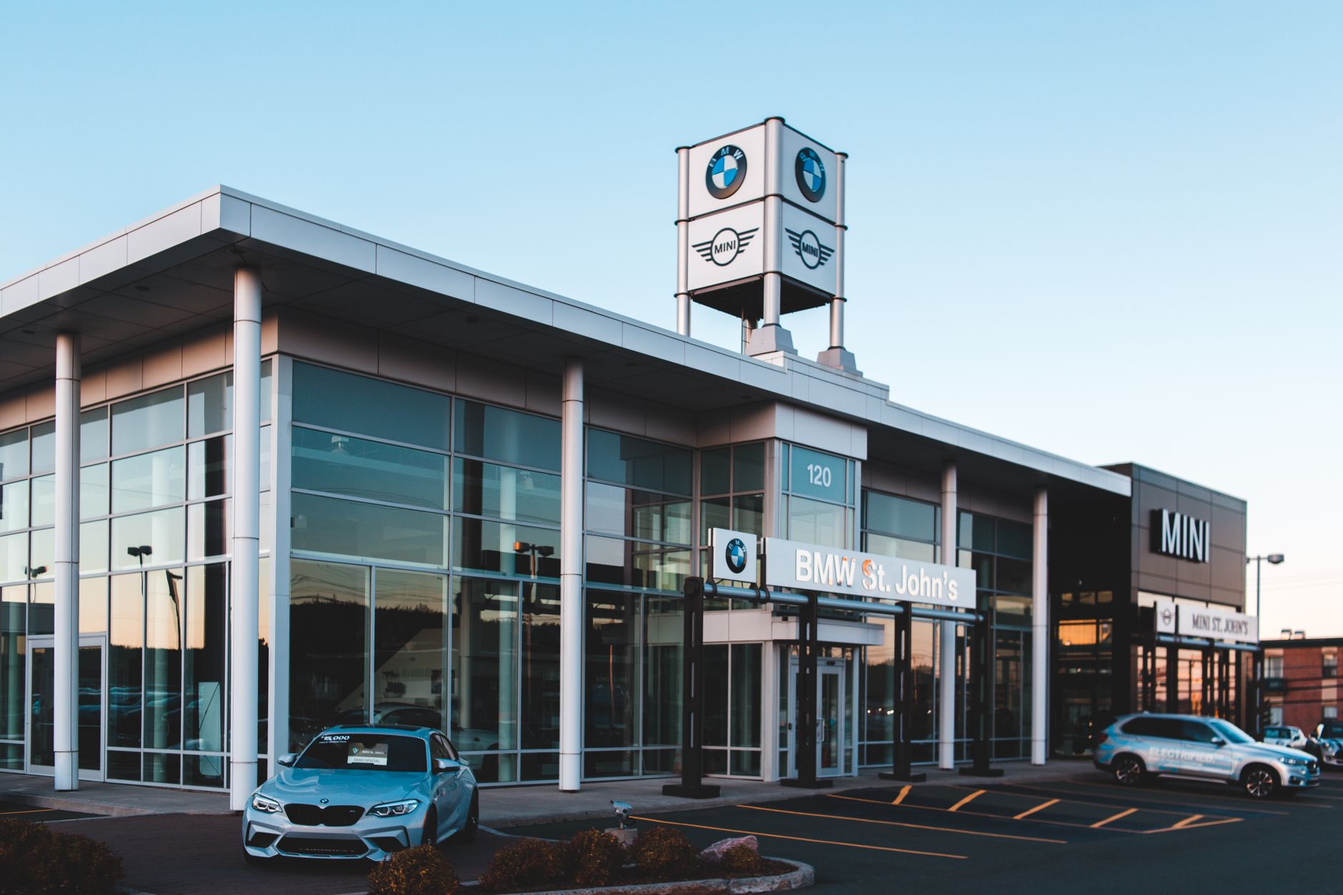 Luxurious car dealership showcasing BMW and MINI cars with a modern glass exterior at dusk.