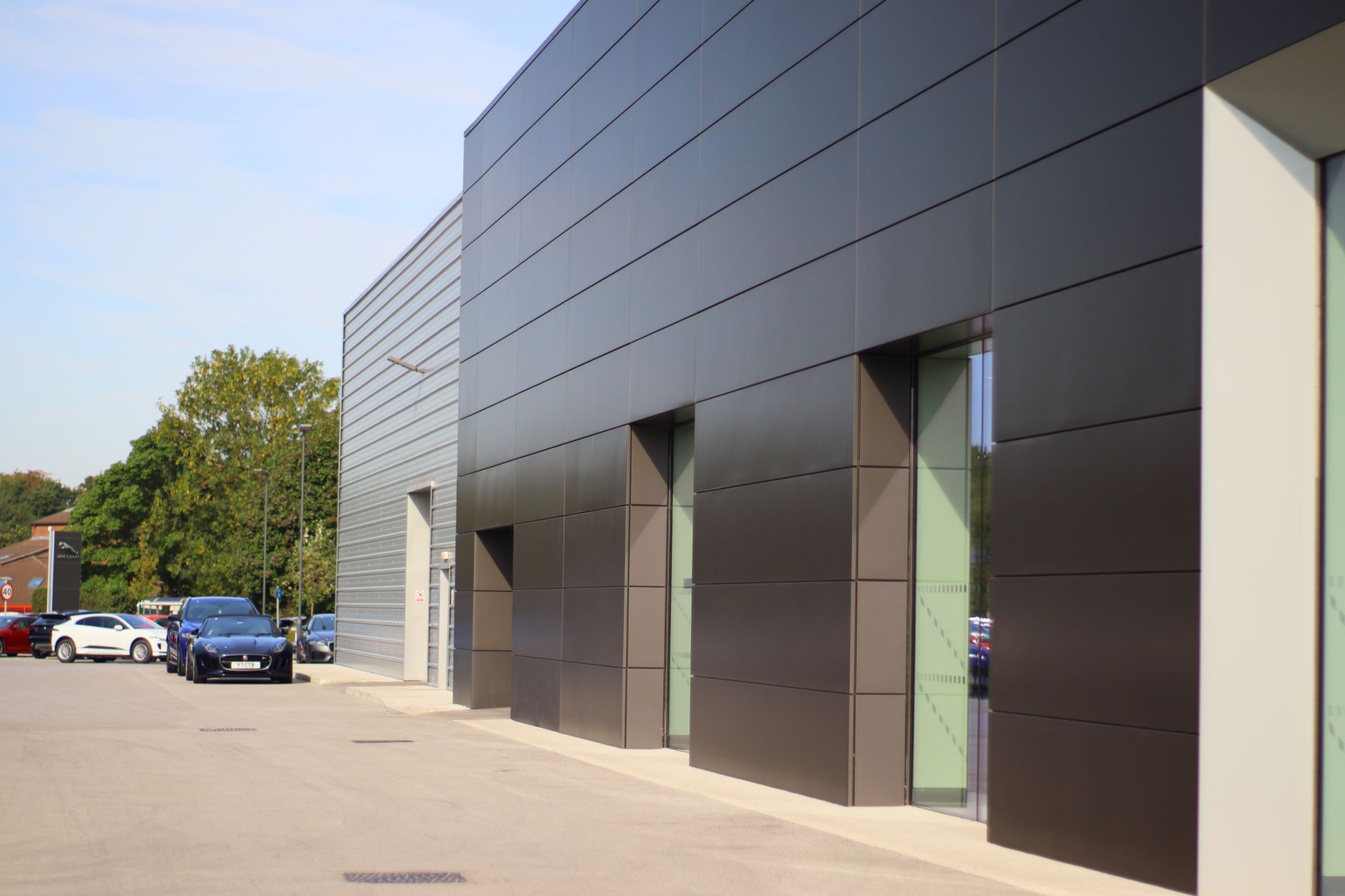 A sleek modern commercial building facade with parked cars under a clear sky.