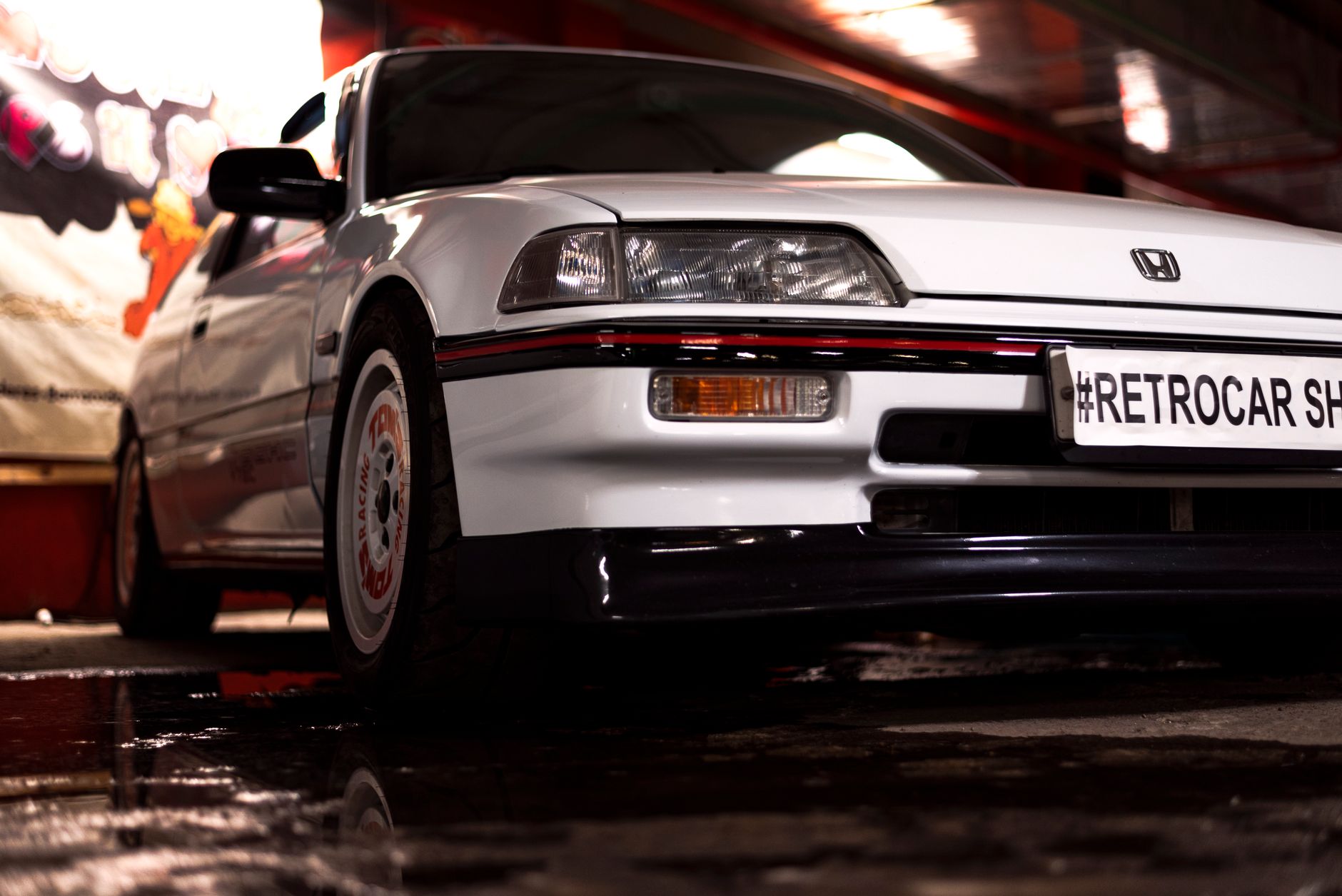 Close-up of a vintage white Honda Civic at a retro car show with reflective puddles.