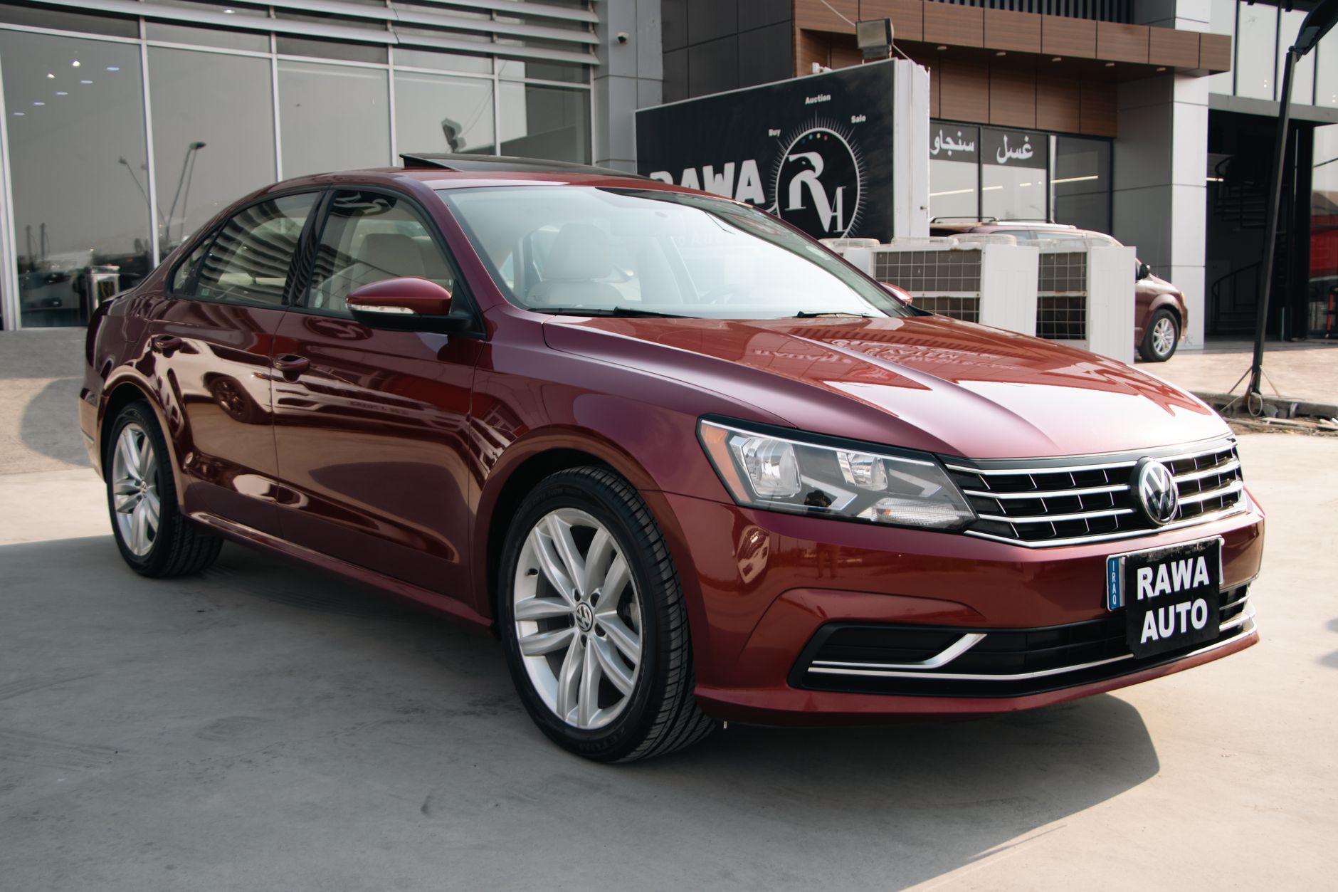 A red Volkswagen Passat displayed at a modern car dealership under daylight.