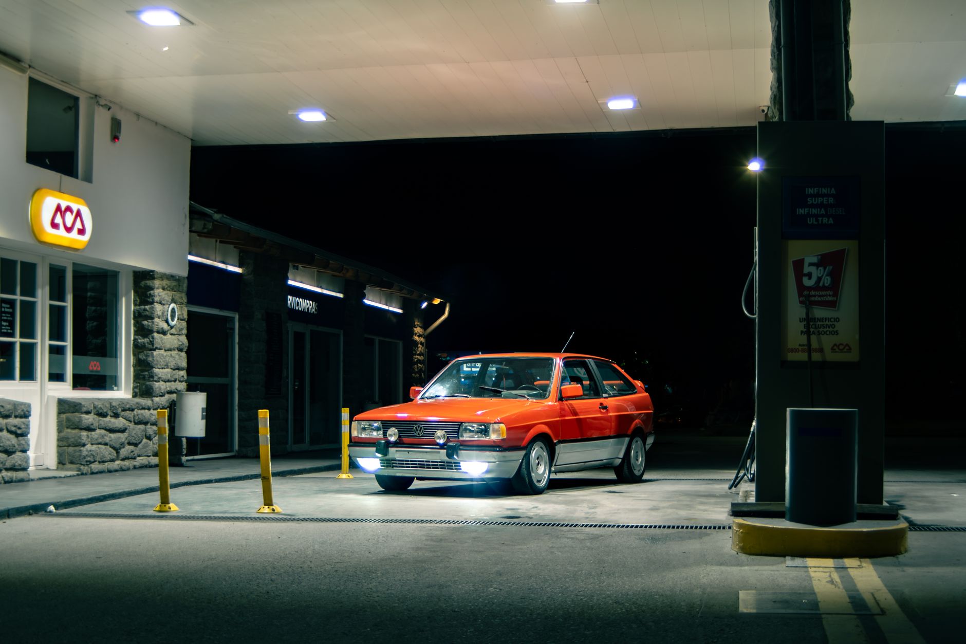 A classic red car at a gas station in El Bolsón, Argentina, at night, showcasing vintage automotive design.