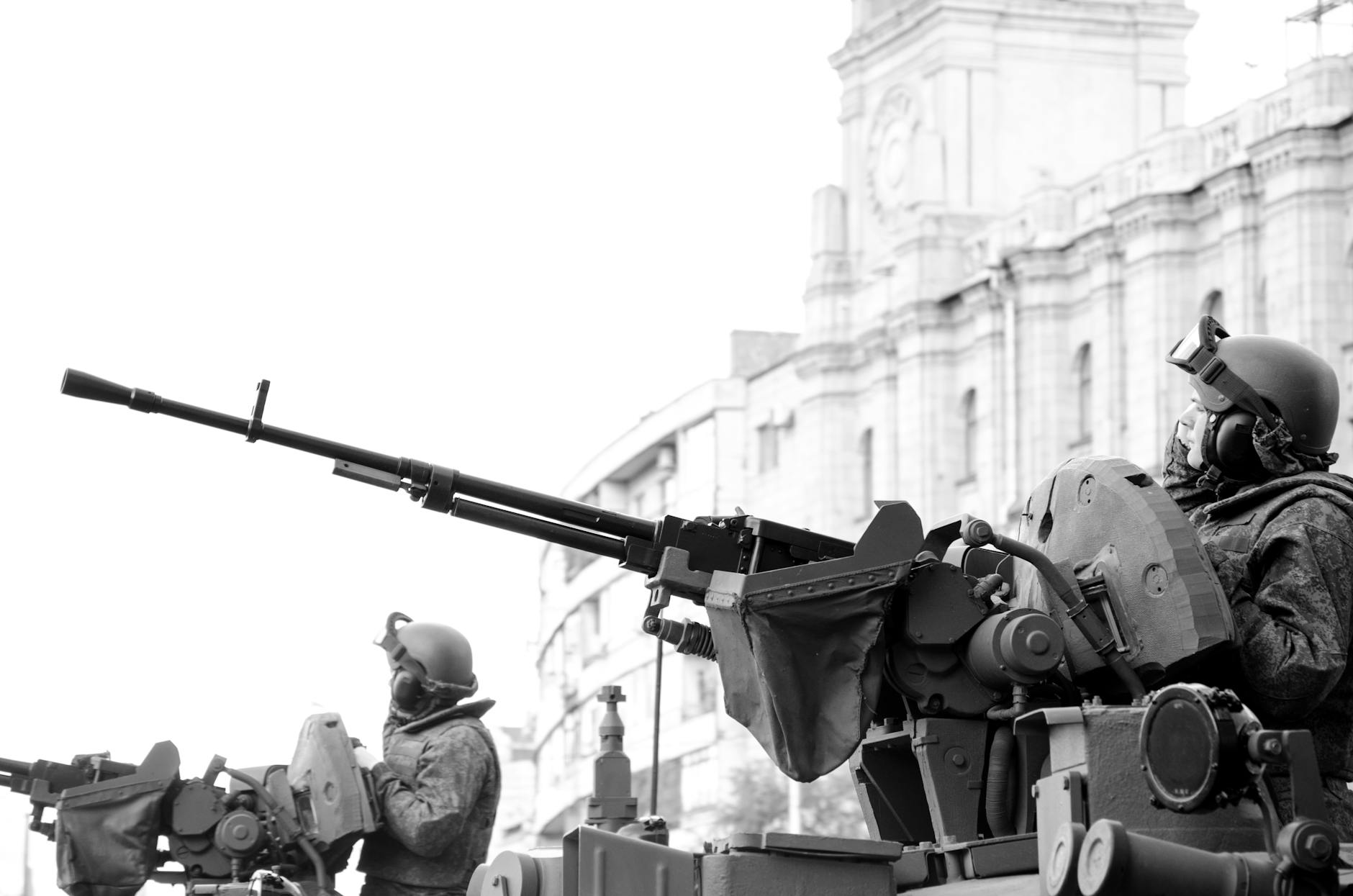 Monochrome image of soldiers in armored tanks, equipped with rifles, patrolling urban surroundings.