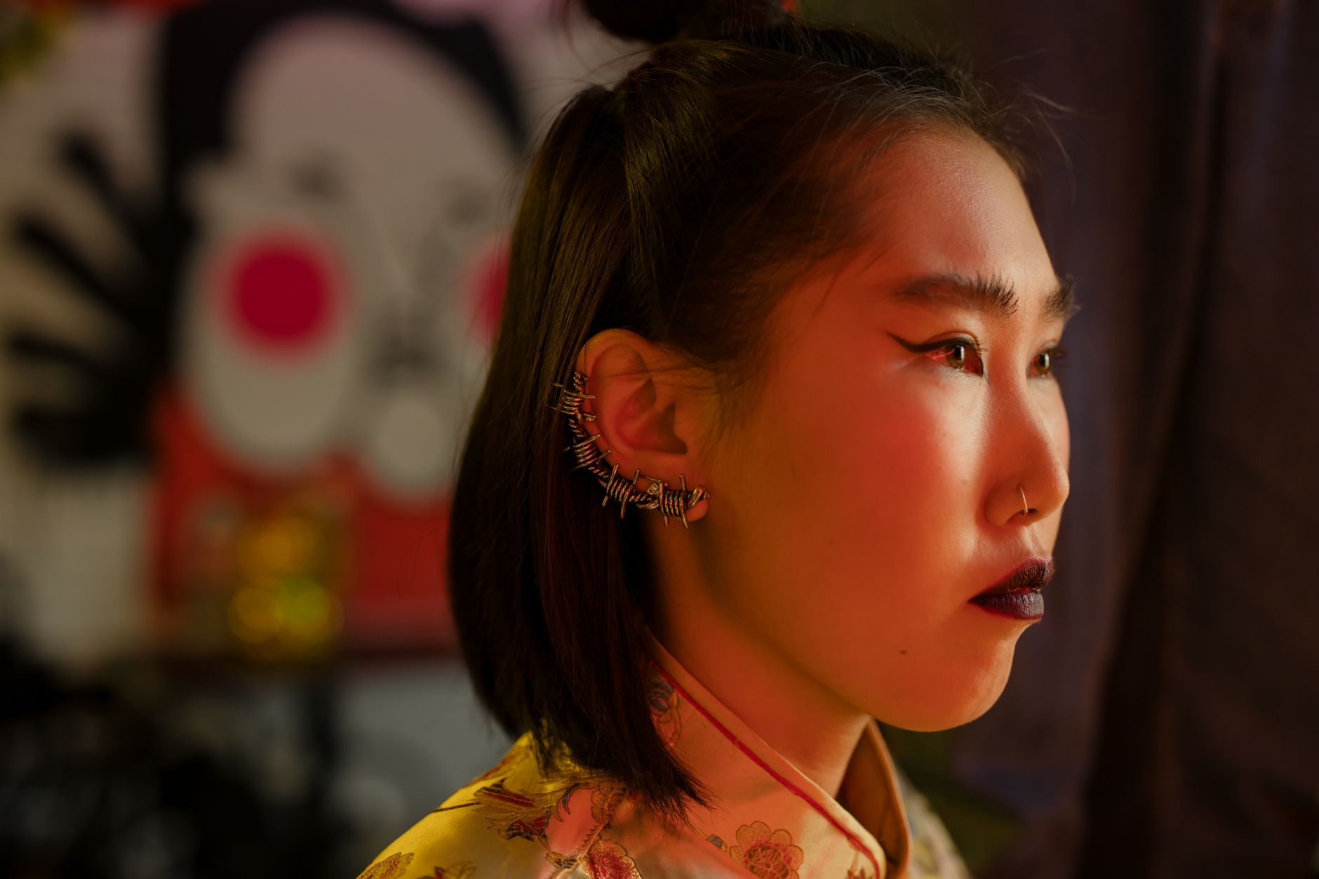 A stylish Asian woman with a distinctive ear cuff and bold makeup in a side profile view.