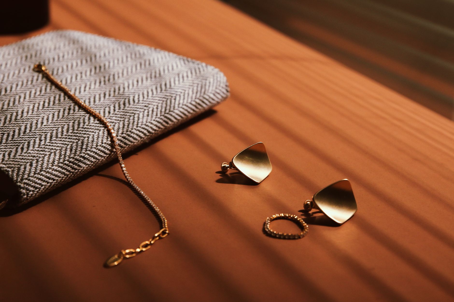 Gold jewelry including earrings and a bracelet beside a stylish clutch on a table.