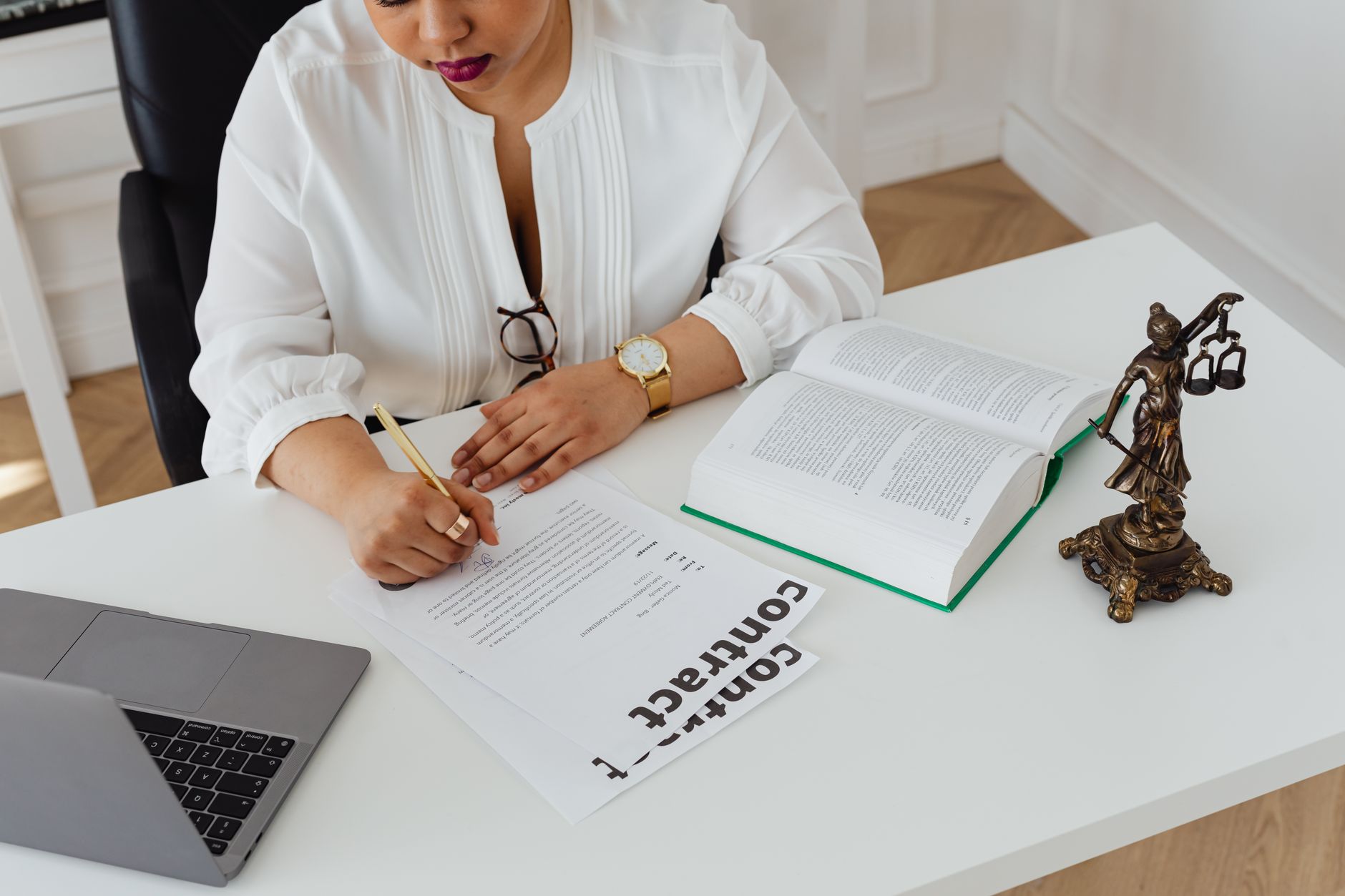 Woman in office writing on contracts, with law books and laptop on table.