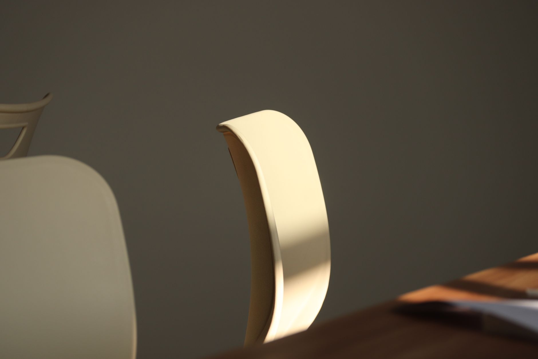 A minimalist office chair in soft sunlight casting dramatic shadows indoors.