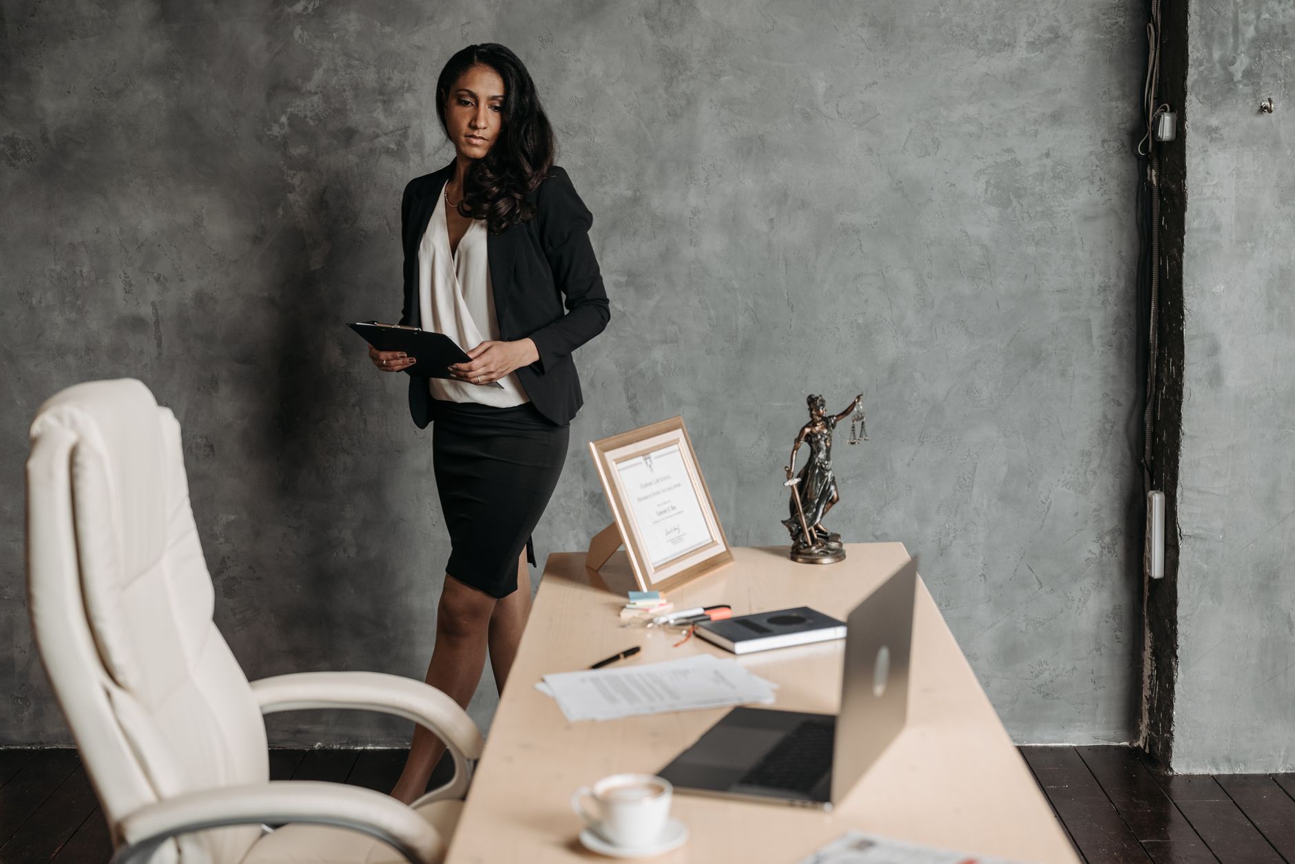 Confident businesswoman in a formal setting with legal papers and a statue of justice on the desk.