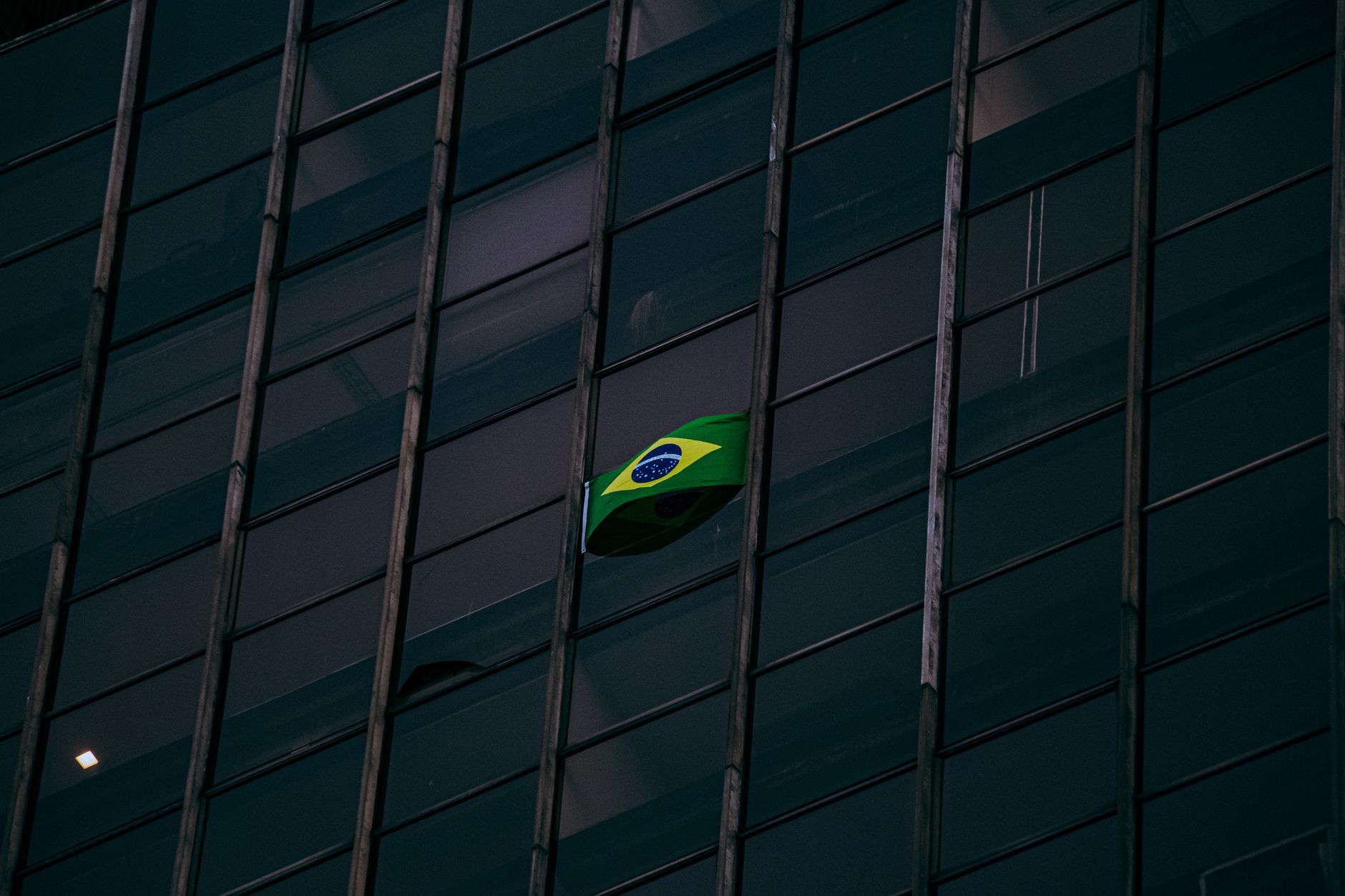Brazilian flag displayed on a modern office building facade at night.