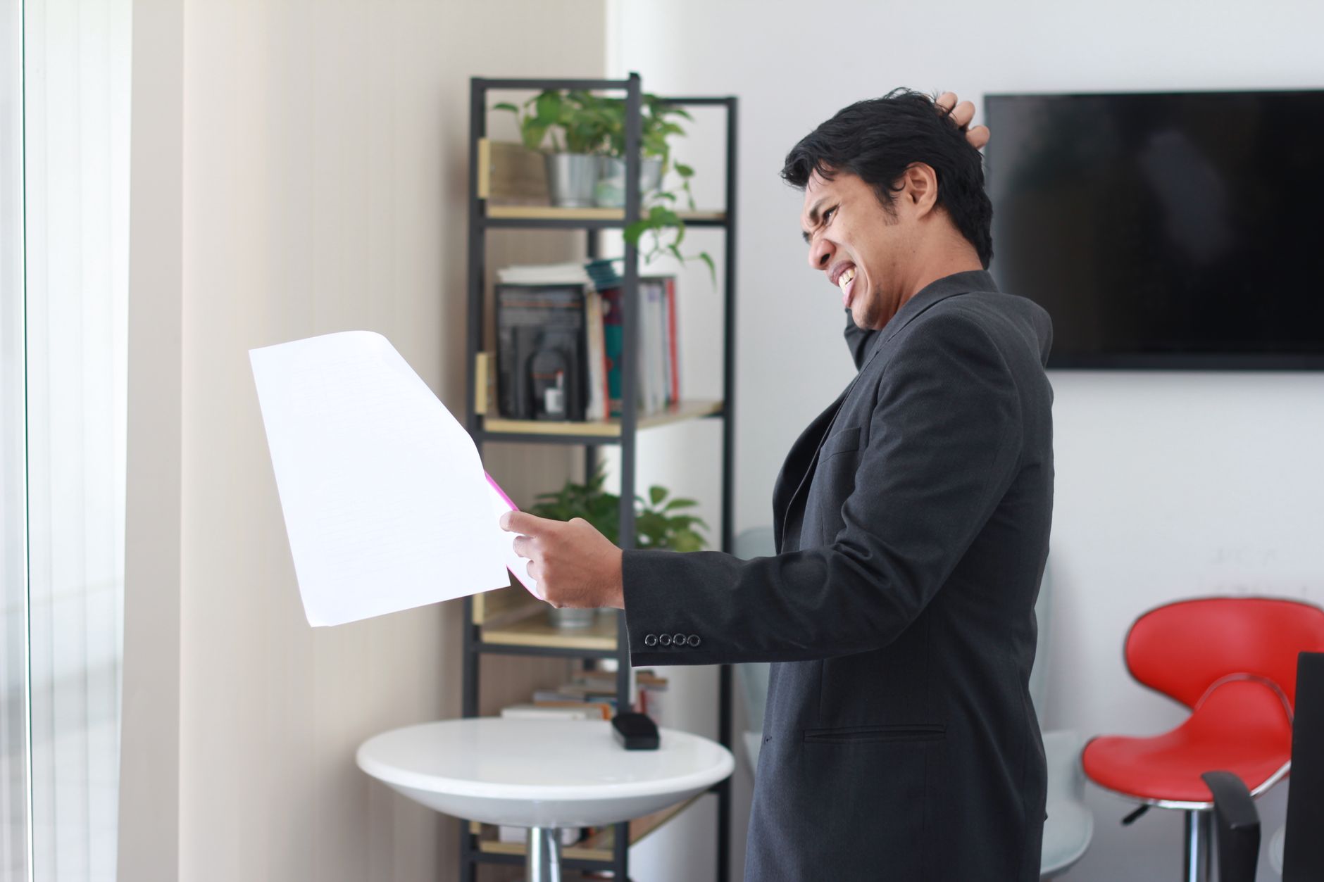 Businessman experiencing stress while holding paper in office.